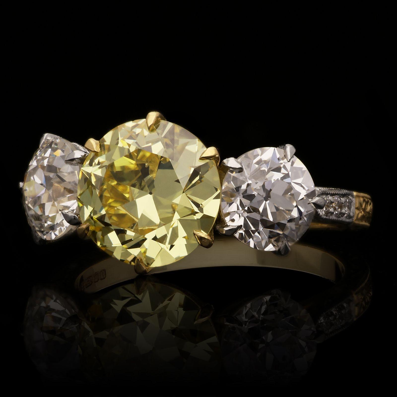 A beautiful old cut fancy coloured diamond and white diamond three stone ring by Hancocks, centred with a wonderful old European brilliant cut diamond weighing 2.41cts and of Fancy Intense Yellow colour and VS1 clarity, claw set in 18ct yellow gold