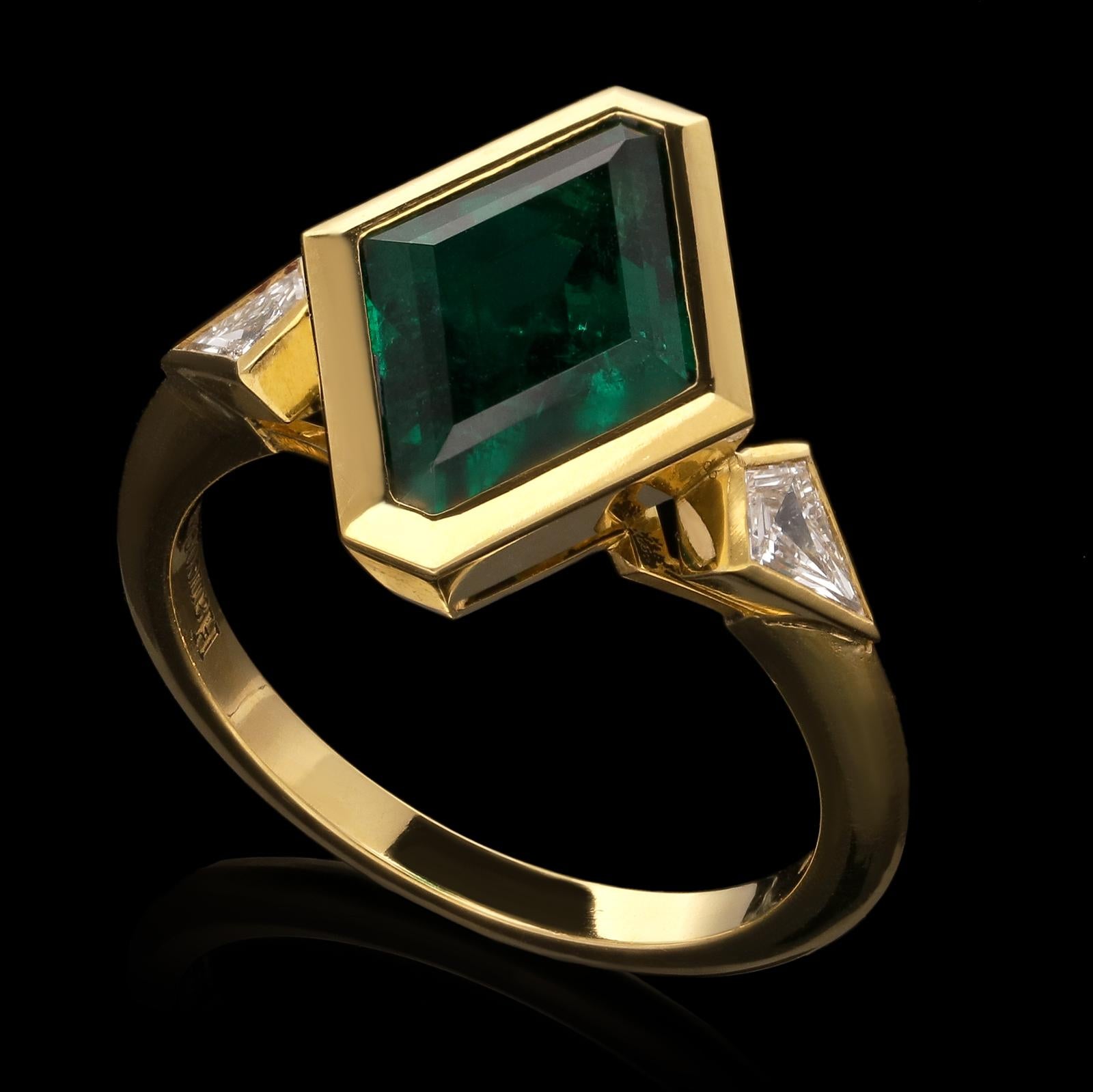 A beautiful lozenge-shape emerald and diamond ring by Hancocks, centred with a step-cut lozenge-shape richly saturated deep green Zambian emerald weighing 2.74ct set within a geometric rub-over bezel setting between shoulders set with kite-shape