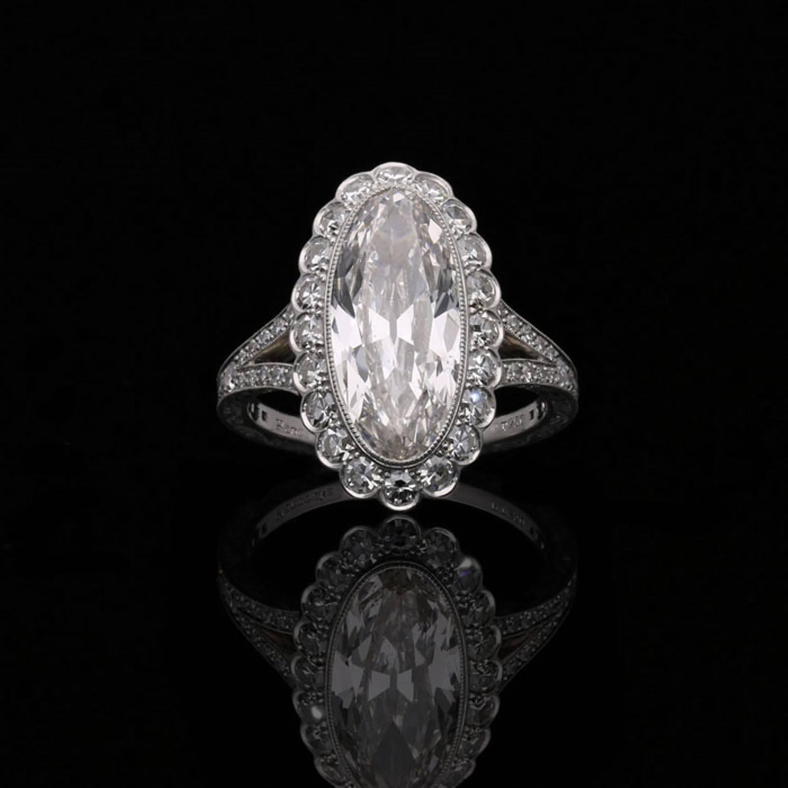 A stunning oval cluster diamond ring by Hancocks centred with a beautiful antique-cut moval shaped diamond weighing 3.35 carat and of H colour and VS2 clarity within a fine millegrained rub-over setting surrounded by a halo of single cut diamonds in