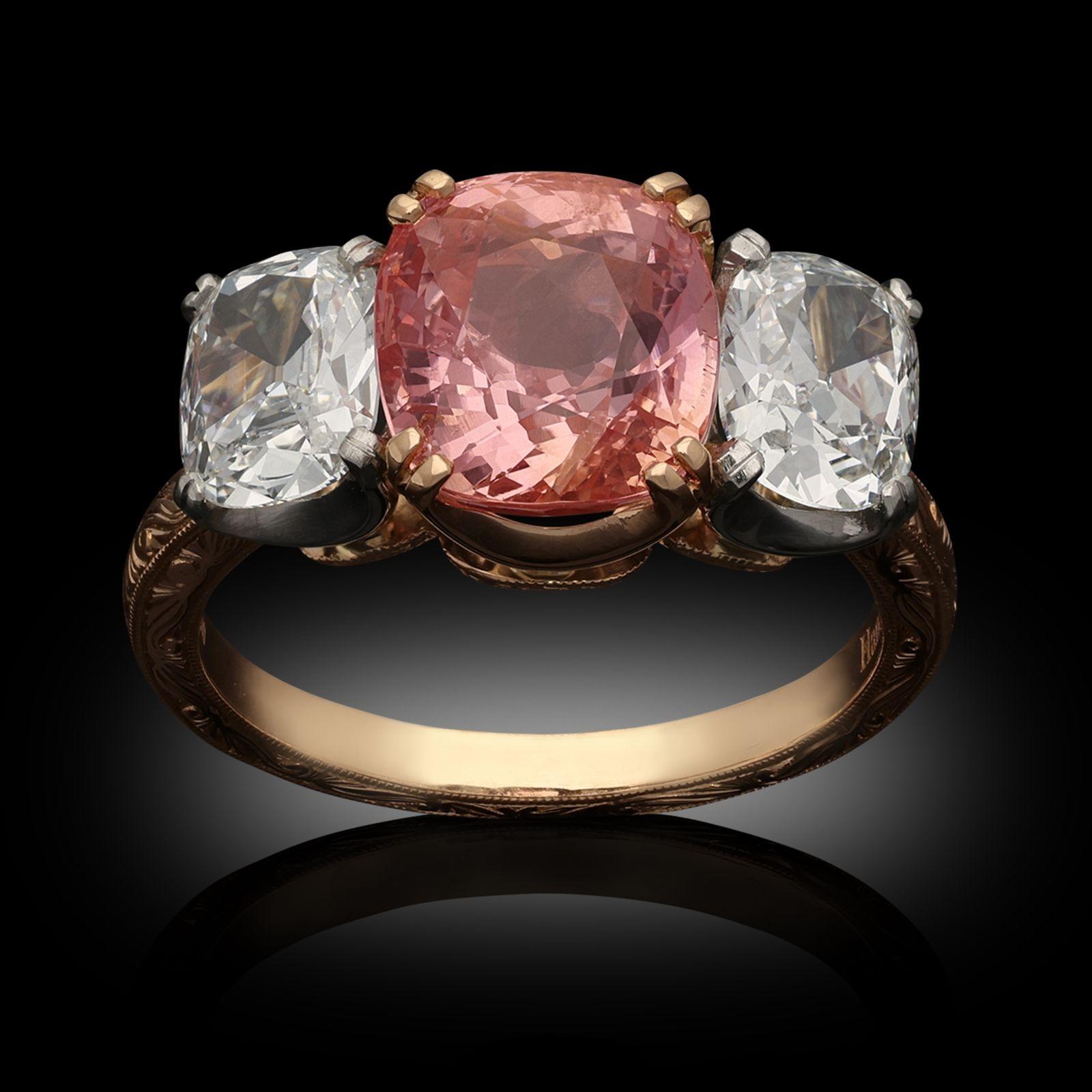 A sapphire and old cut diamond three stone ring by Hancocks, set to the centre with a beautiful cushion shaped Ceylon padparadscha sapphire weighing 4.16cts claw set in 18ct rose gold between two old mine cushion cut diamonds, one weighing 0.73ct