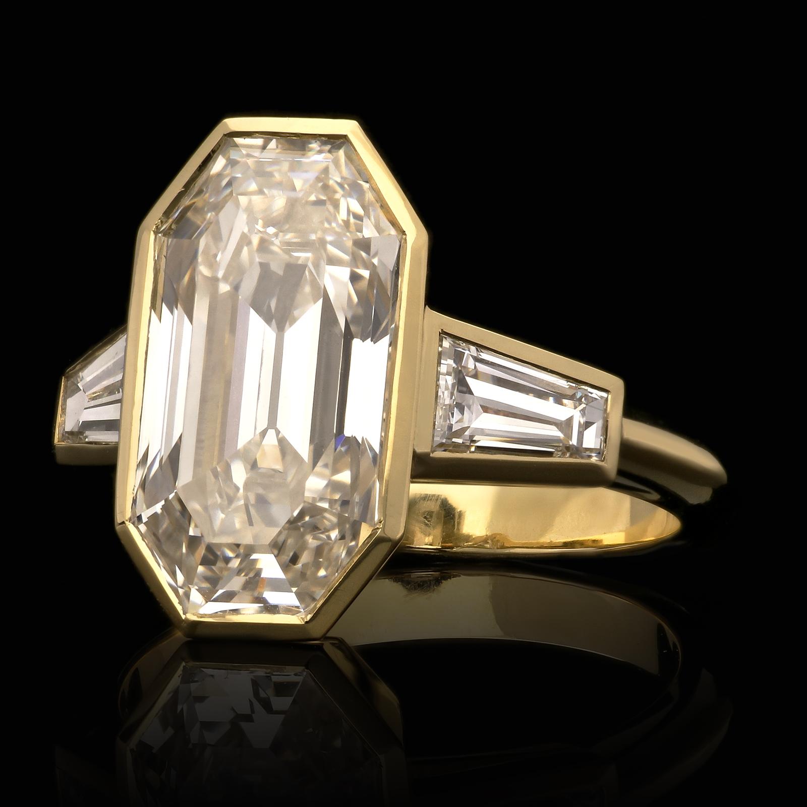 A beautiful emerald cut diamond bezel set ring by Hancocks centred with an old emerald cut diamond weighing 5.38ct and of I colour and VVS1 clarity in a fine bezel setting of 18ct yellow gold set between shoulders of tapered baguette diamonds