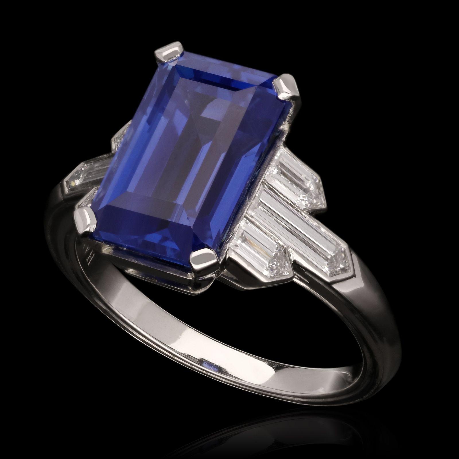 A beautiful sapphire and diamond ring by Hancocks, centred with an emerald-cut unheated Ceylon sapphire weighing 6.19cts and corner claw set between shoulders of three bullet cut diamonds in rub over settings, all in a finely crafted platinum mount