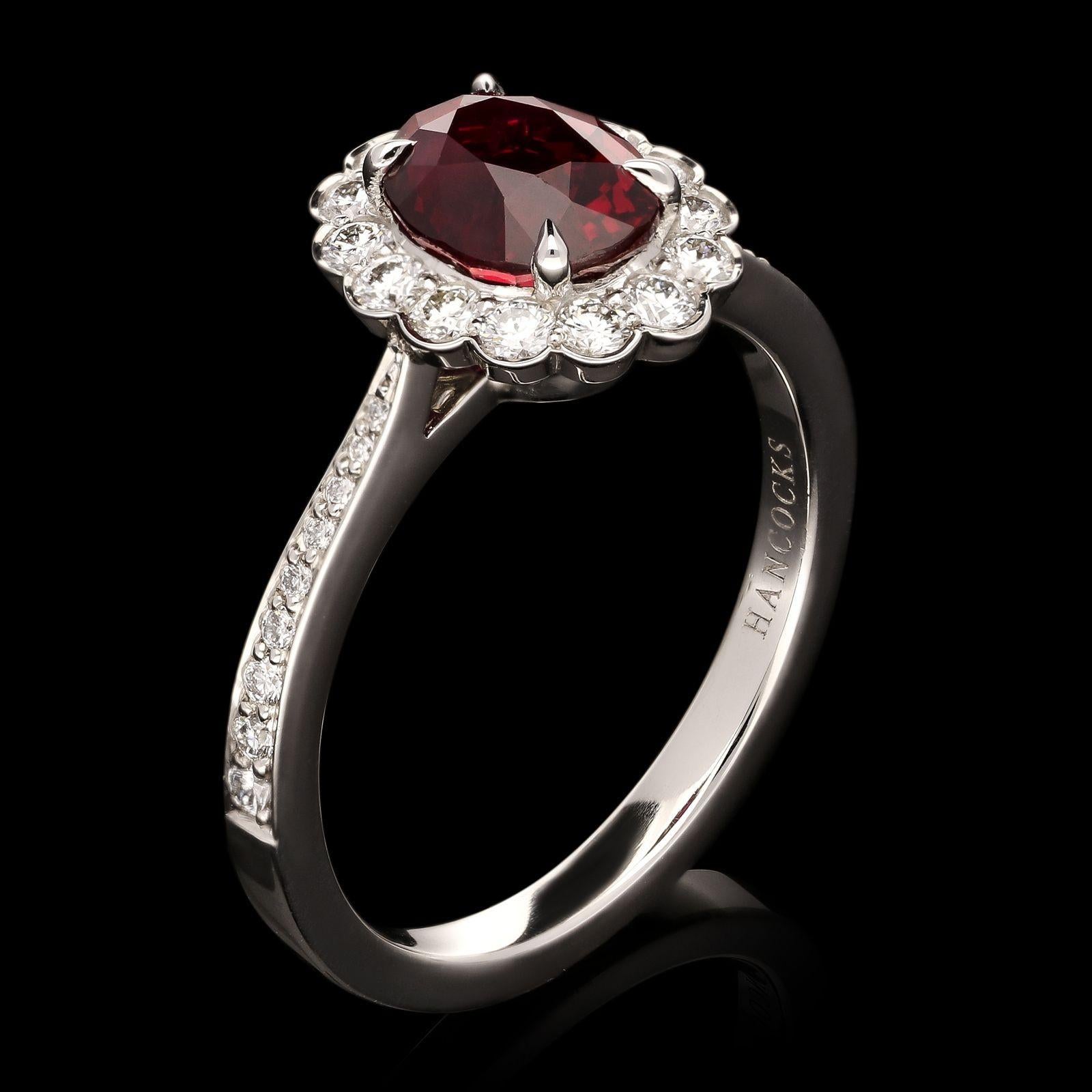 A classic oval ruby and diamond cluster ring by Hancocks, centred with a beautiful oval ruby weighing 1.57cts claw set within a cluster surround of round brilliant cut diamonds in scalloped setting between finely tapering shoulders set with round