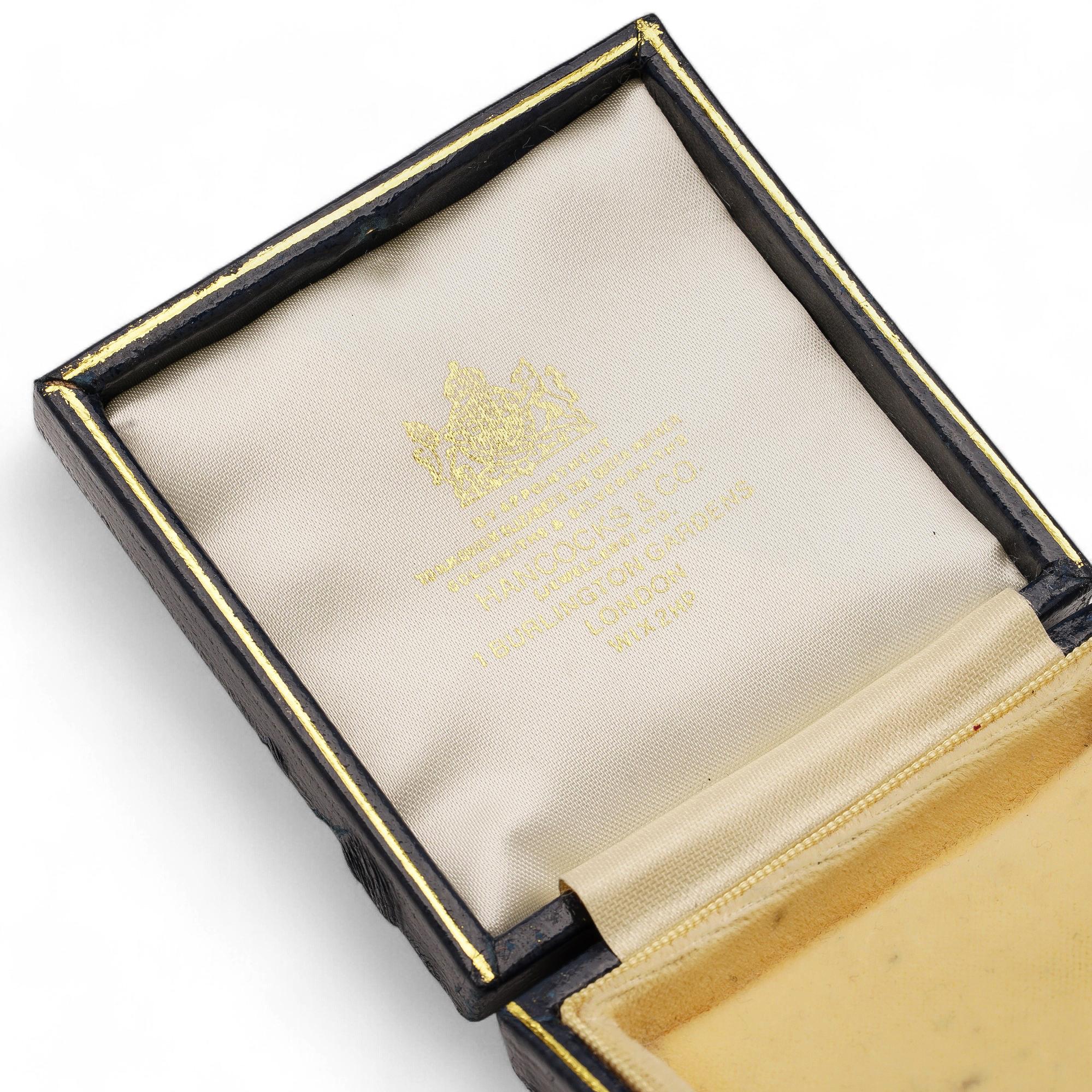 Une boîte à broches carrée au design compact. L'extérieur a une finition mate, tandis que l'intérieur présente un velours doux avec une doublure de couvercle en satin, offrant une présentation élégante.

Une boîte à broches vintage de Hancocks & Co.