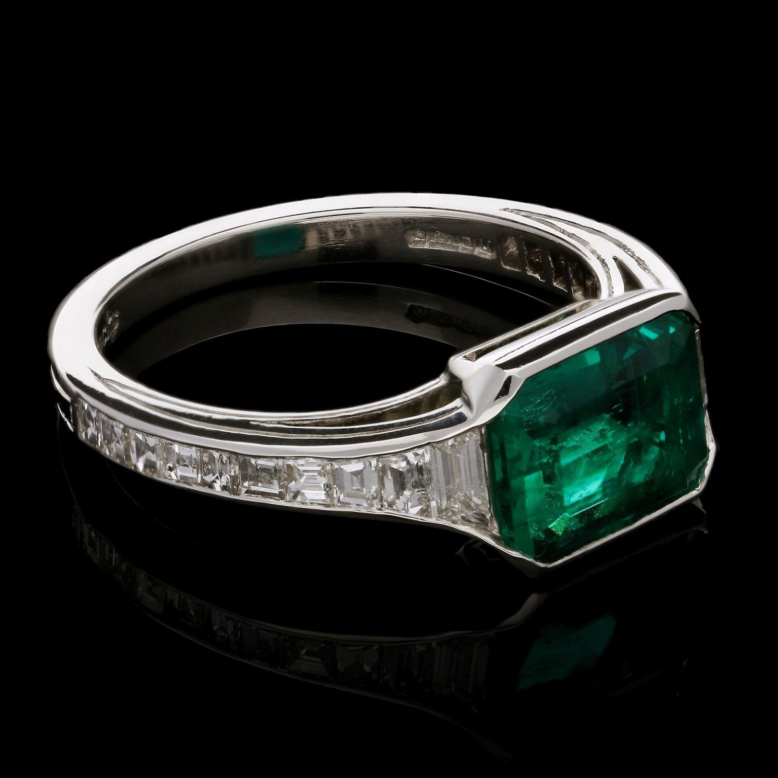 An elegant emerald and diamond ring by Hancocks set horizontally to the centre with an emerald-cut emerald in rubover setting between tapering shoulders set with calibre step-cut diamonds, all in a finely handcrafted platinum