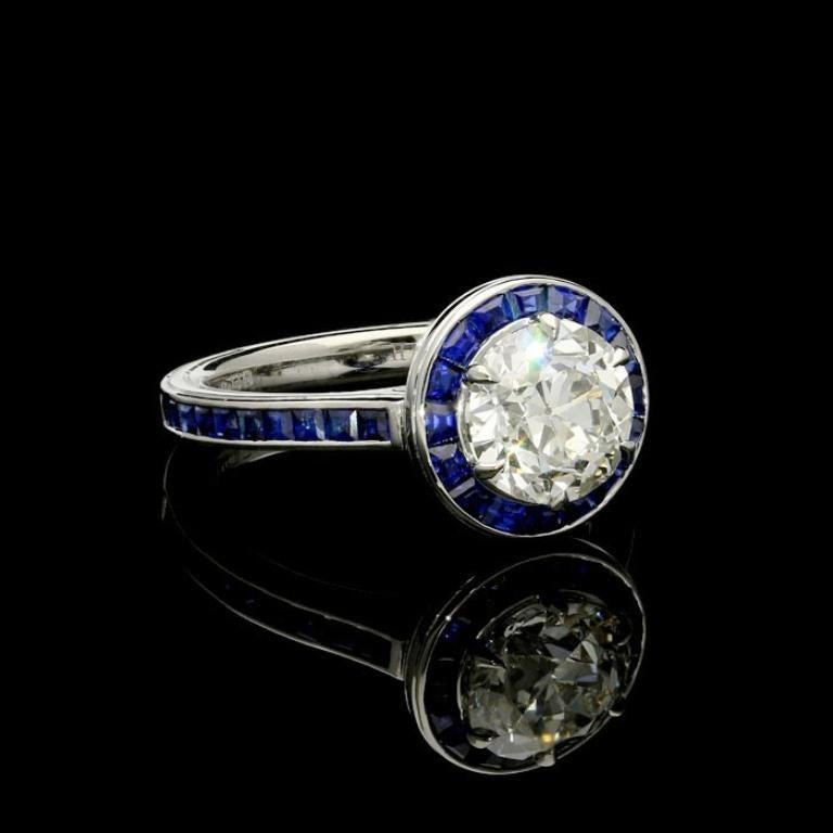 A beautiful old cut diamond and sapphire halo ring by Hancocks, centred with a bright and lively old European cut diamond weighing 2.02ct and of J colour and VS1 clarity claw set within a halo surround of calibre cut sapphires in a channel setting