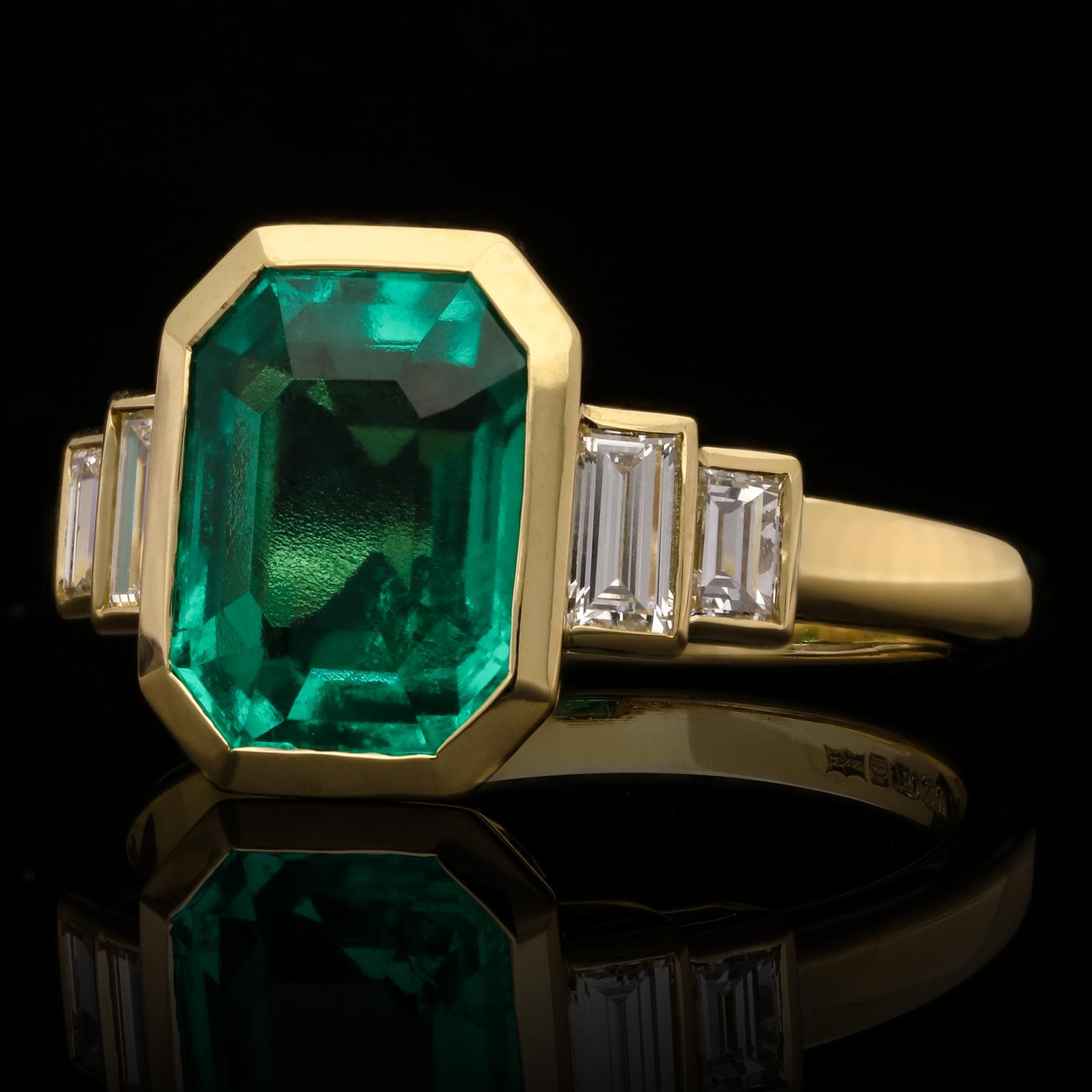A beautiful emerald and diamond ring by Hancocks, centred on a lovely rich and deeply saturated emerald-cut emerald of Colombian origin weighing 2.41cts rub over set in 18ct yellow gold between elegant stepped shoulders set with baguette cut