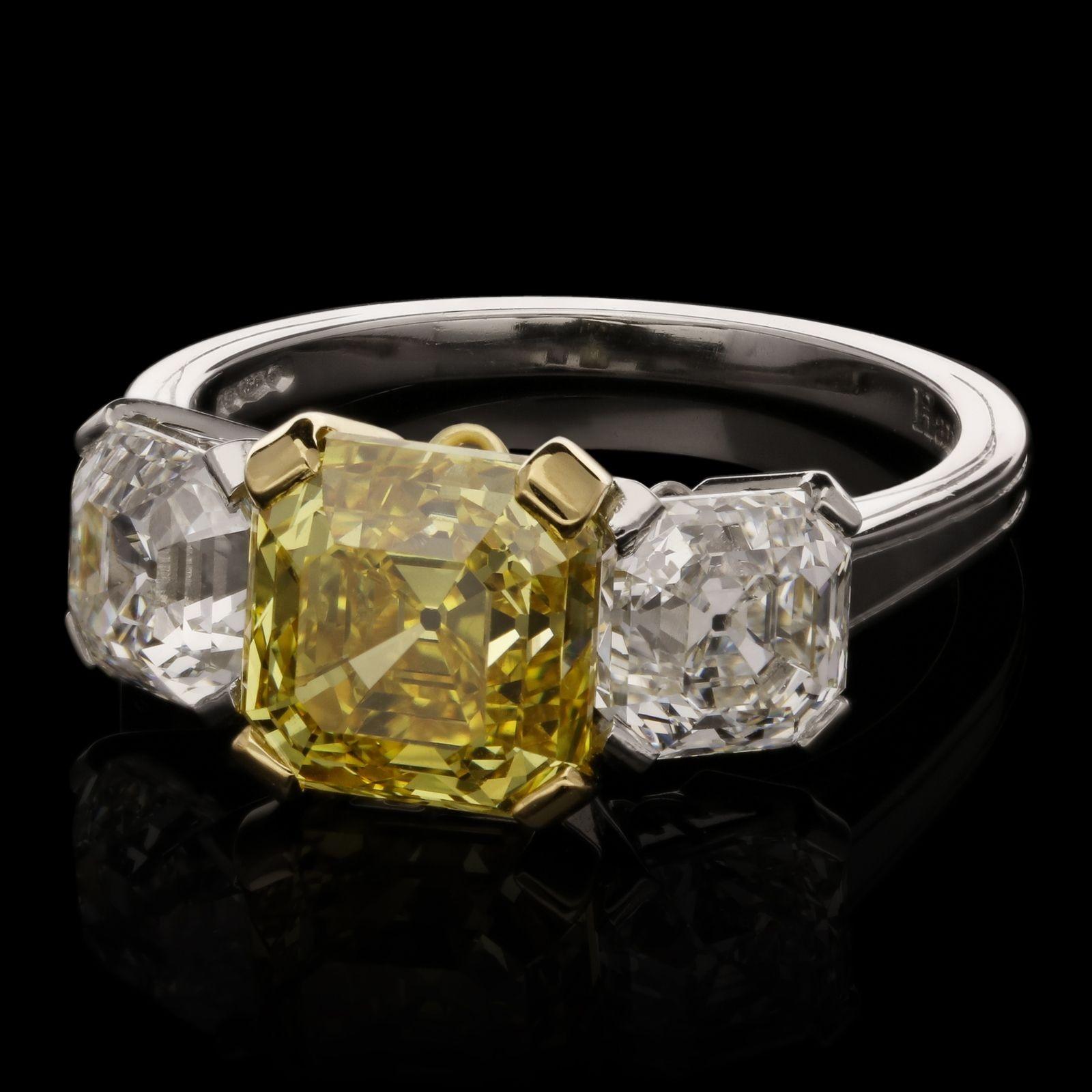 A beautiful diamond and fancy colour diamond three stone ring by Hancocks, set to the centre with an Asscher cut fancy vivid yellow diamond weighing 2.94cts and of VVS2 clarity in an 18ct yellow gold corner claw setting, between two Asscher cut