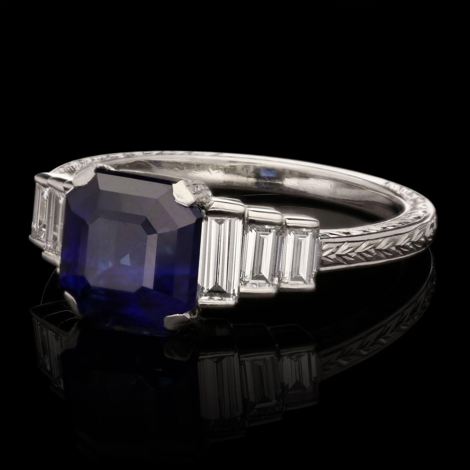An elegant sapphire and diamond ring by Hancocks, centred with a natural unheated emerald-cut  sapphire weighing 2.80cts, corner claw set East to West between shoulders set with three graduated and stepped baguette cut diamonds in partial rub over