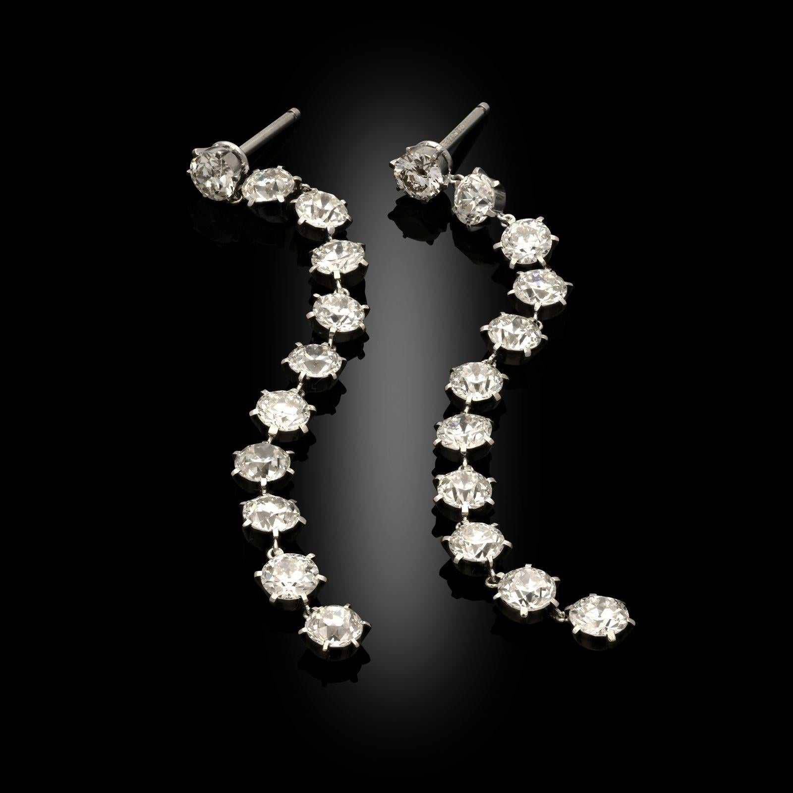 A pair of old cut diamond drop earrings by Hancocks. These earrings are designed as a single long line of old European cut diamonds, each in platinum claw set mount with articulation between each diamond. Each earring has eleven diamonds with the