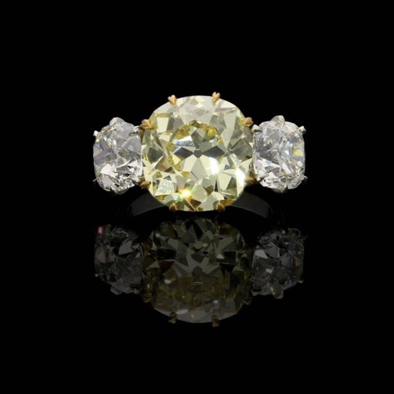 An exceptional three stone diamond and Fancy Intense yellow diamond ring by Hancocks, set to the centre with a beautiful old mine brilliant cut yellow diamond weighing 8.28 carats and of fancy intense colour and VS2 clarity claw set in yellow gold