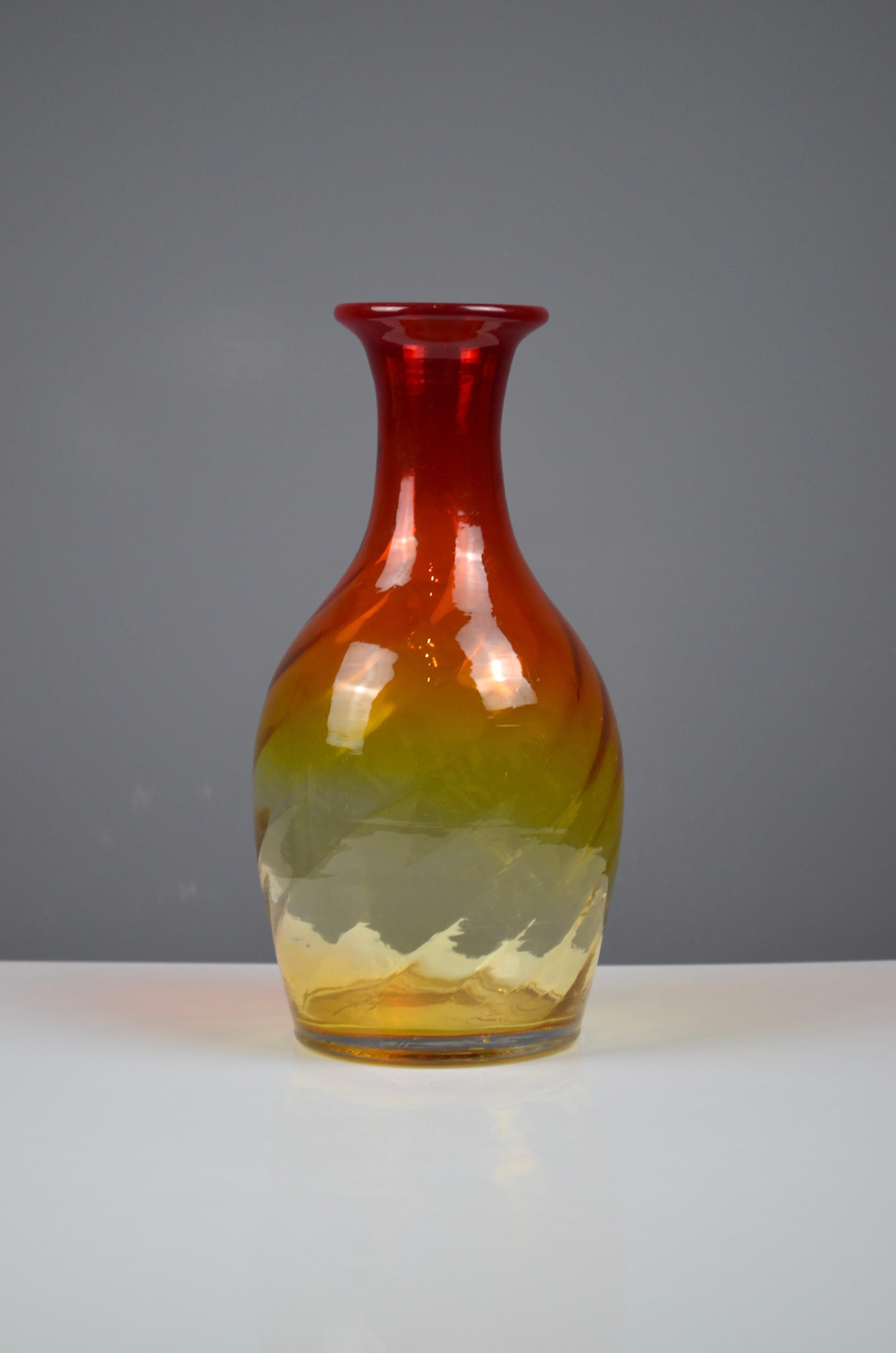 A striking hand-blown art glass vase with amberina gradient, fading beautifully from deep ruby red at the neck to warm amber yellow at the base. 
 The glass has been subtly twisted while hot, creating a gentle spiral movement within the body that