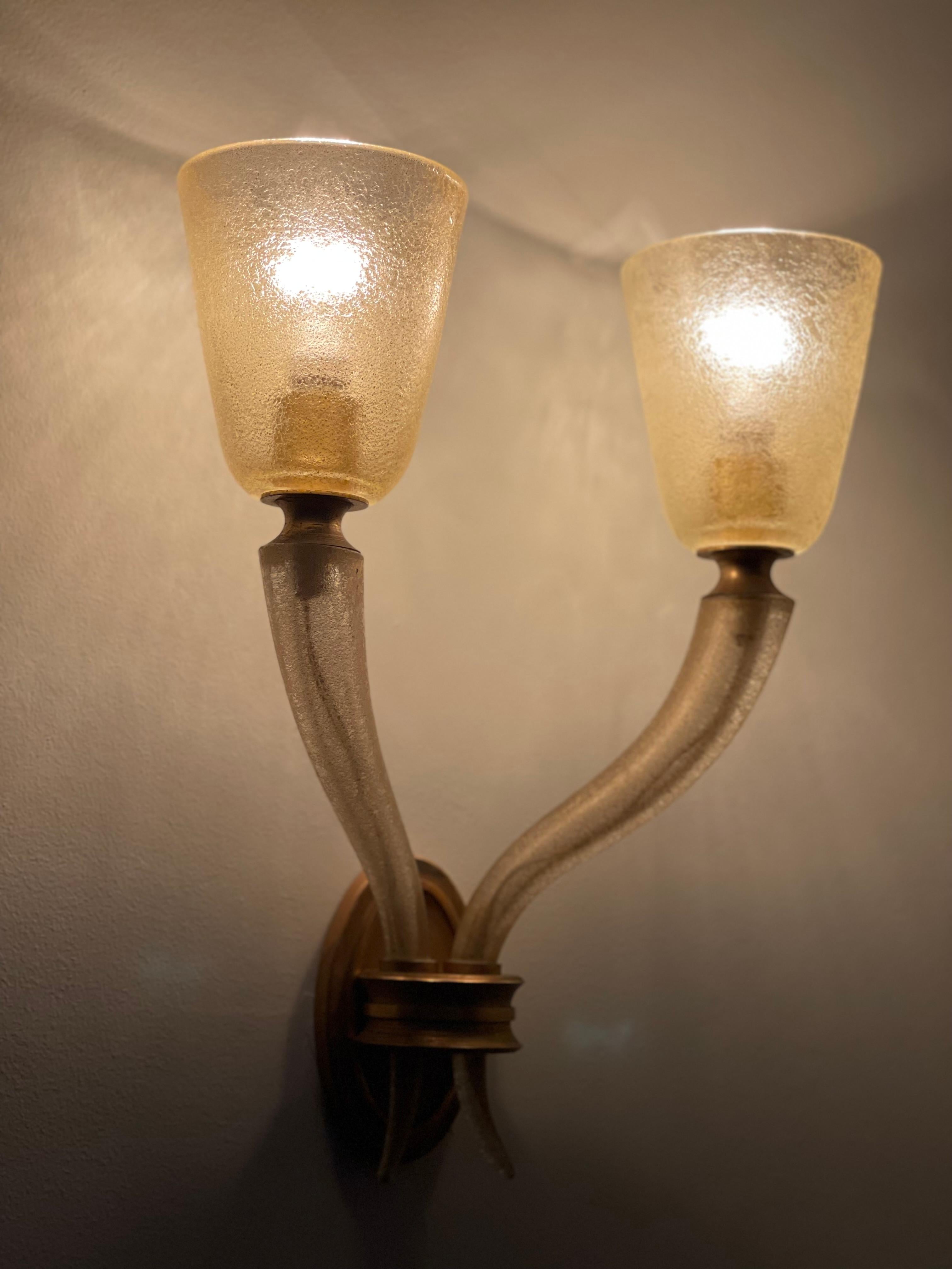 Lampe murale en laiton et verre de Murano des années 1940. Les abat-jours en verre ont une finition en Corroso avec des feuilles d'or.

L'applique est équipée de 2 ampoules Pin 15 w [incluses et envoyées avec la lampe].

Bon état avec seulement de