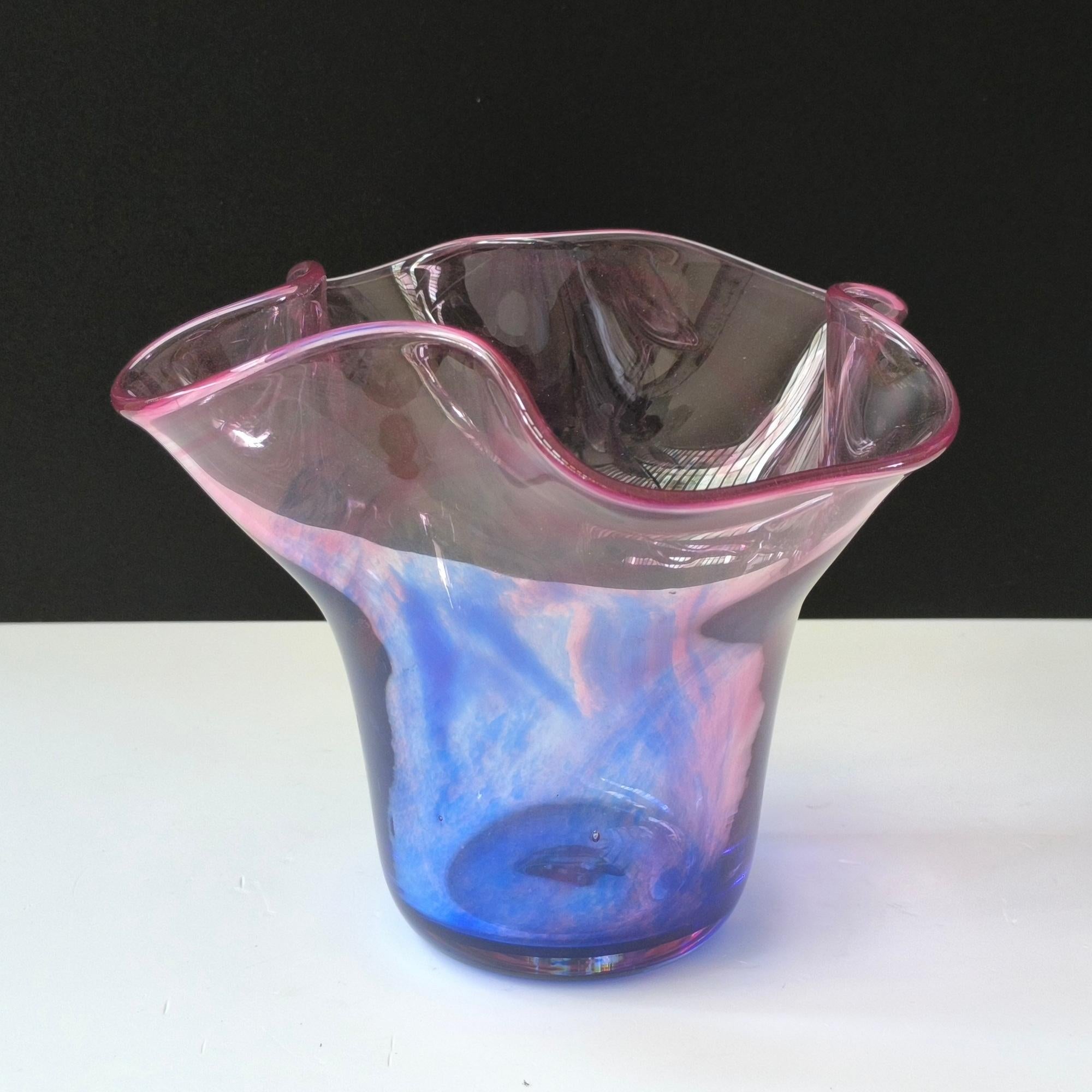 Diese exquisite Vase aus mundgeblasenem Kunstglas ist ein meisterhaftes Beispiel für Studio-Glasdesign, das künstlerische Form und funktionale Eleganz nahtlos miteinander verbindet. Mit ihrem einzigartigen, gewellten, skulpturalen Rand, der an eine