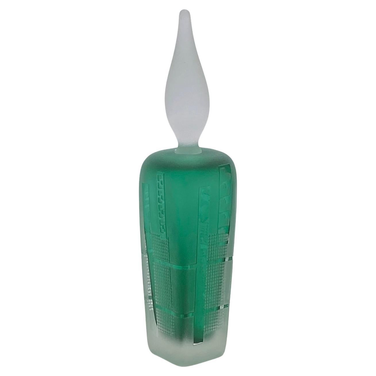 Se trata de un frasco de perfume de vidrio artístico soplado a mano. El cuerpo verde escarchado de la botella está grabado con motivos geométricos de alta tecnología. Lleva un delantal de vidrio esmerilado en forma de llama de vela. Firmado Grant en