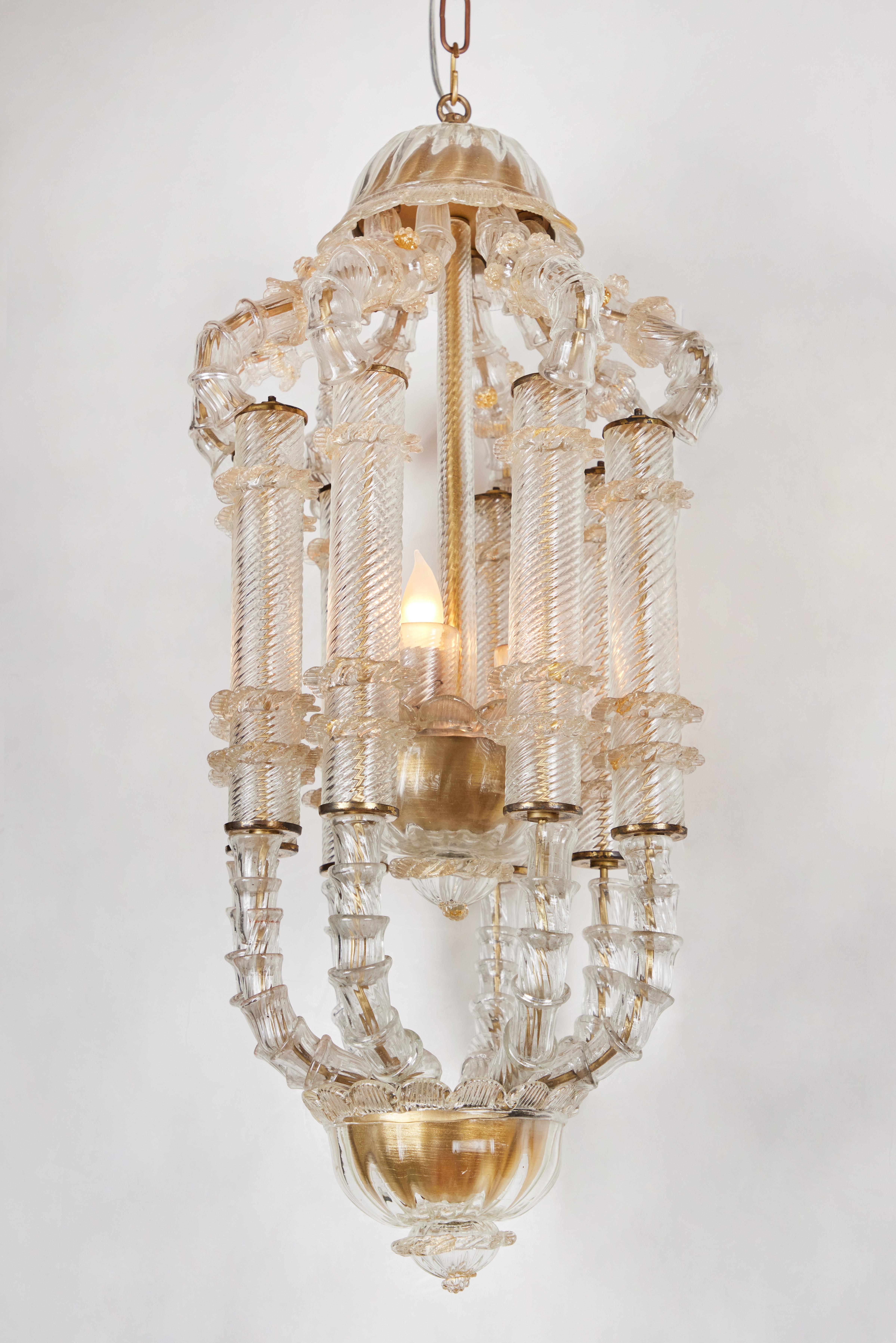 A detailed, Venetian glass lantern featuring a center circle of rigadin columns trimmed in foliate style embellishments between upper and lower registers of elegant supports with raised details. The crown, center dish, and base are fitted with gilt