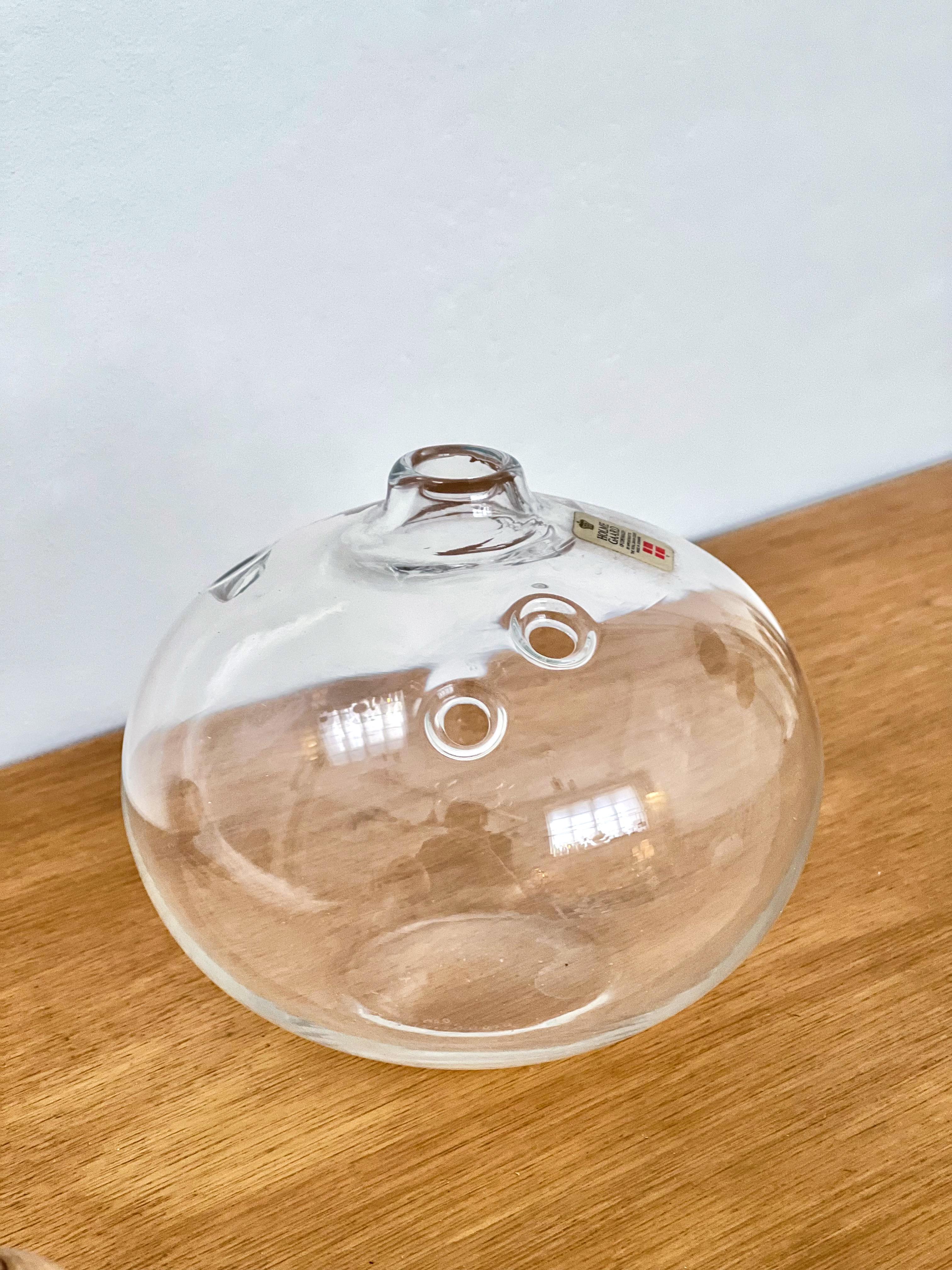Mouth blown clear glass Hull (hole) vase, called the Meteor Vase
Designed by Michael Bang for Holmegaard, Denmarkt, 1970s. Produced between 1973-1978. 
The transparent glass of the body are added of the holes that give breath to the internal