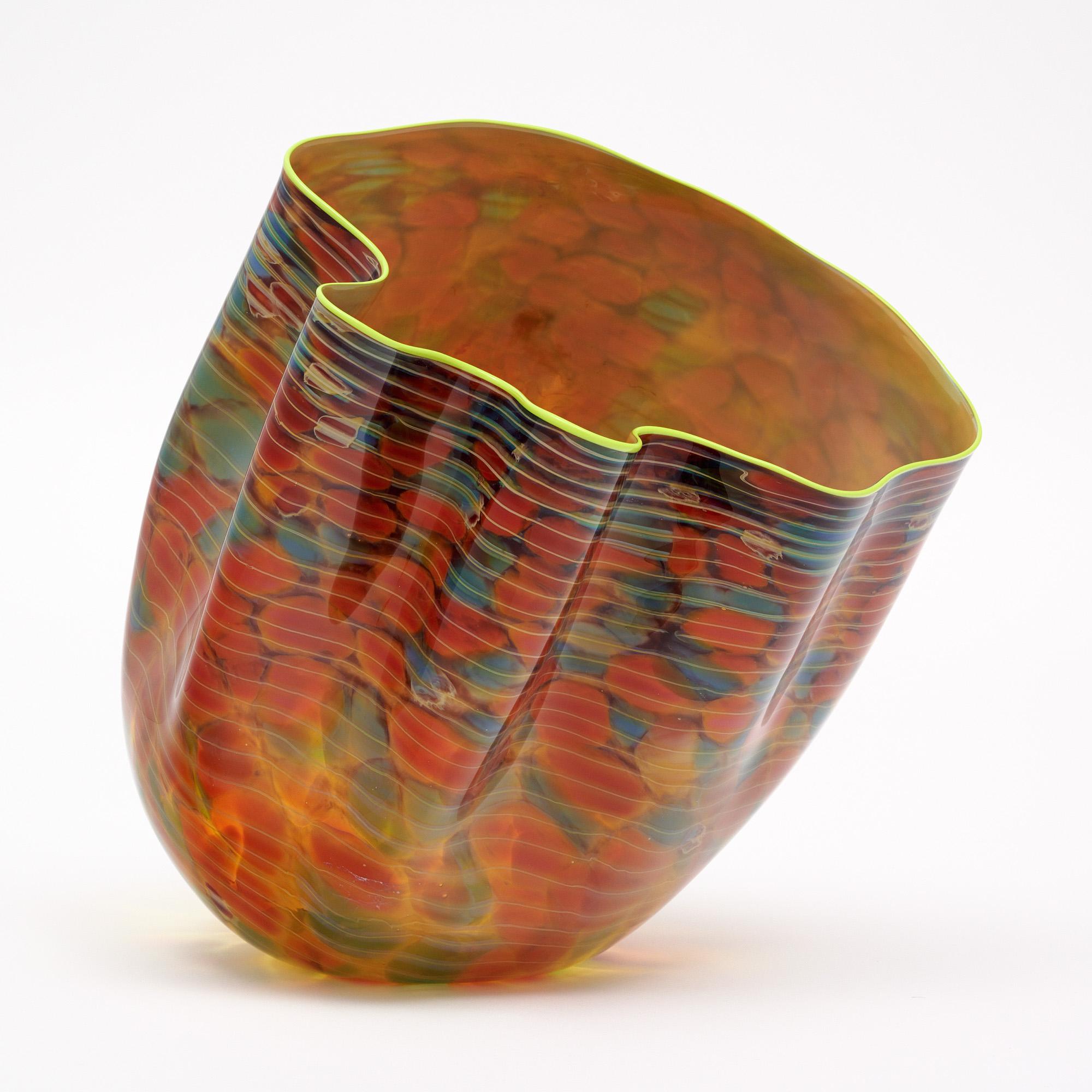 Hand-blown glass vase by renowned glass artist Dale Chihuly. This piece has lovely red and green tones with a neon yellow rim. We love the organic, asymmetrical shape. This piece is in very nice condition – the photos accurately depict the condition.