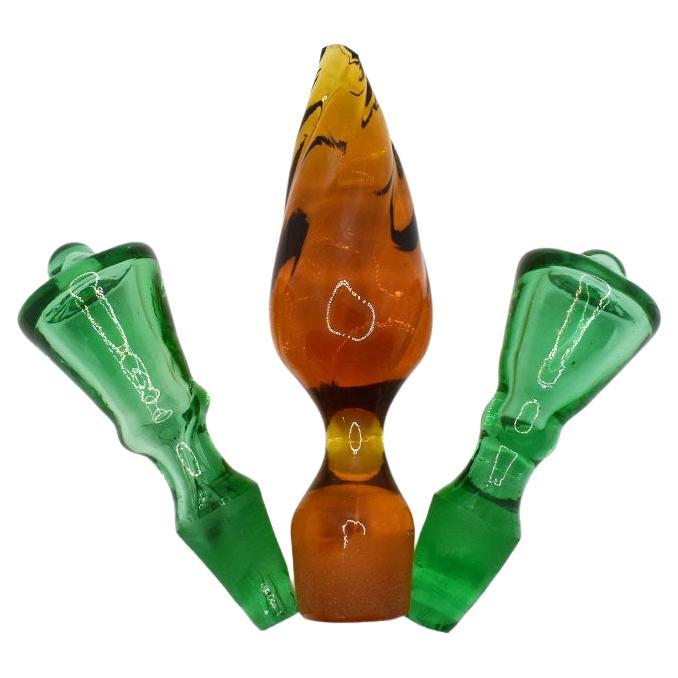 A set of three vintage hand-blown art glass bottle stoppers in emerald green and brown. This set of three includes two emerald green stoppers and one larger brown stopper. They are teardrop in shape and have an inner bubble. A great way to add color