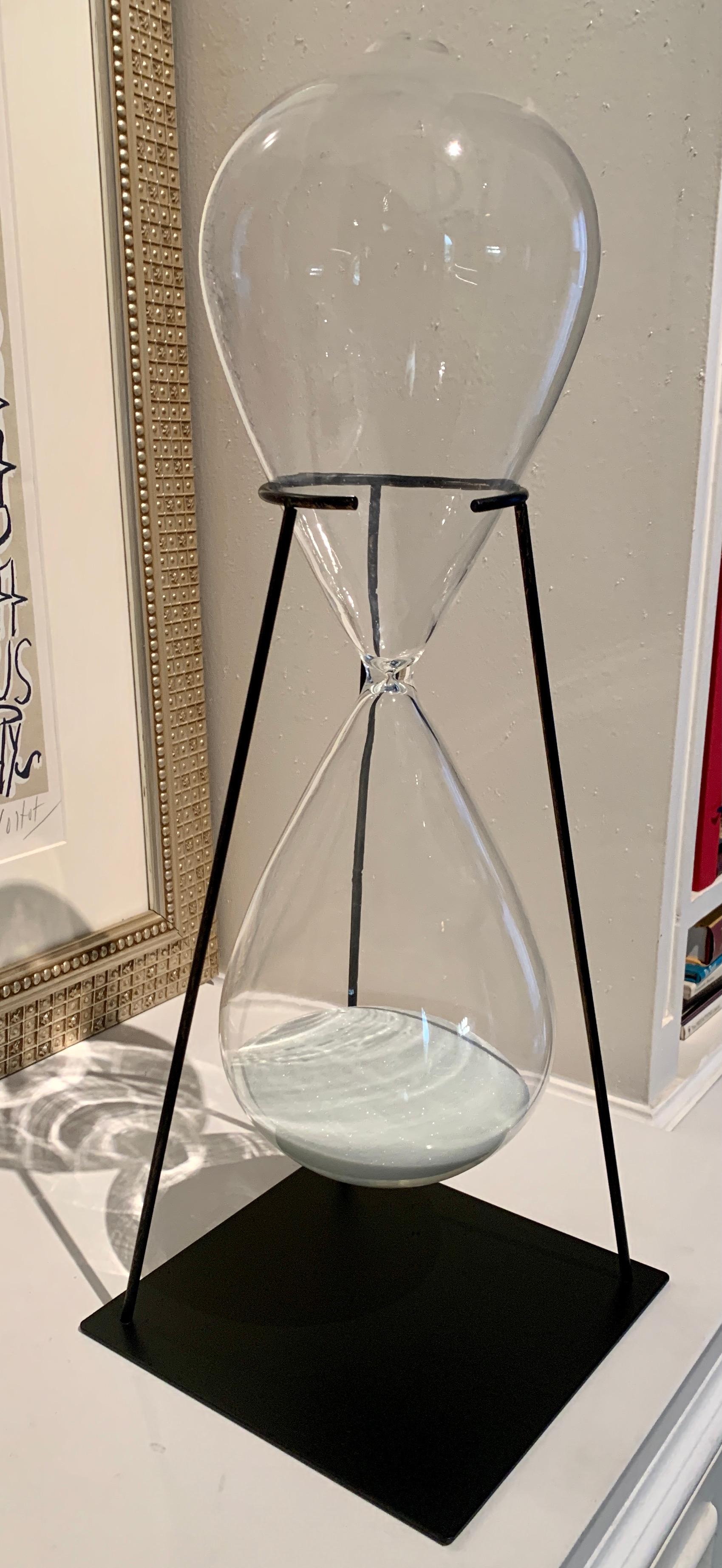 An hour glass on a custom stand - the piece keeps time at about 50 minutes, however is far more decorative than practical. A unique and hand crafted metal stand holds this hand blown glass hour piece. A perfect compliment to any shelf, or a