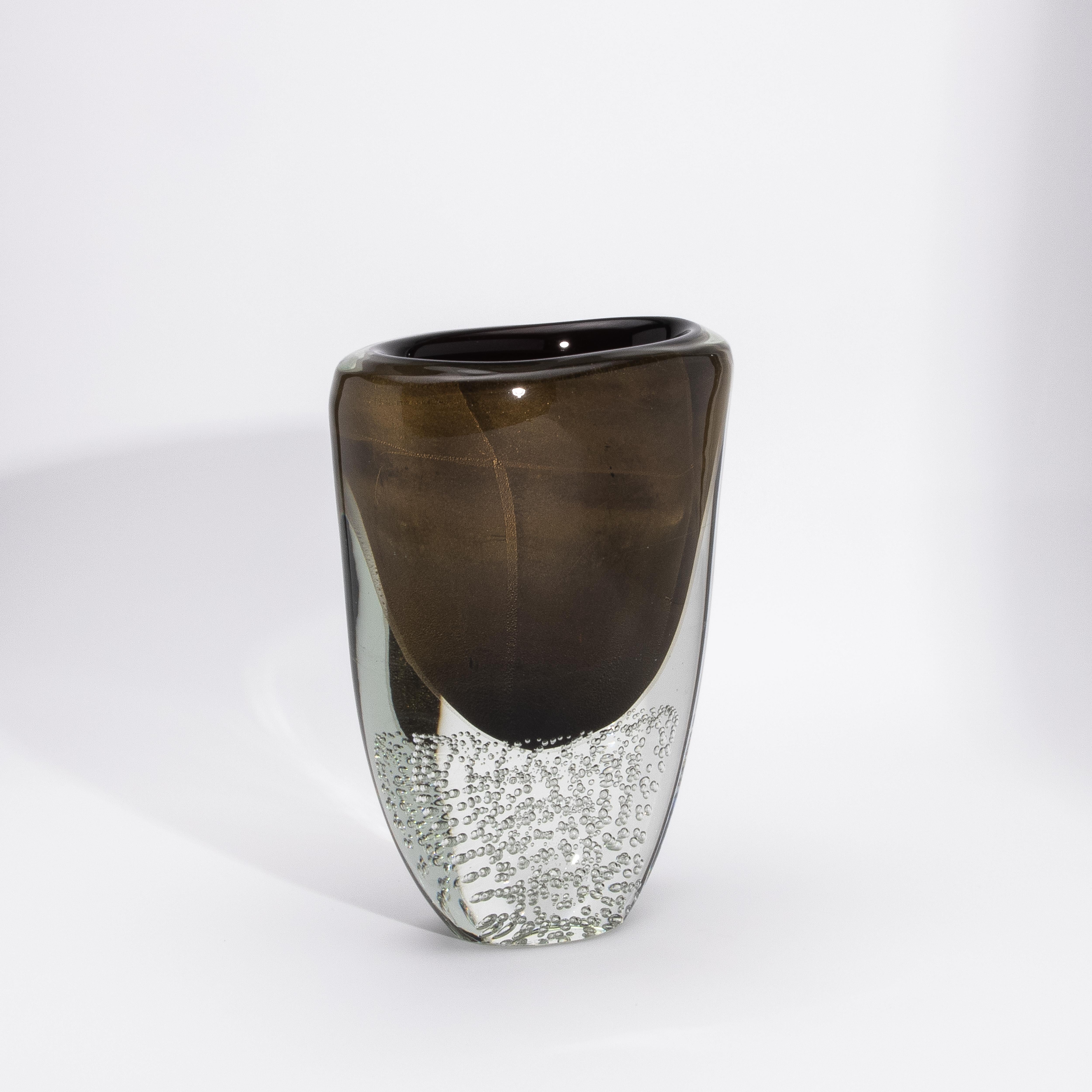 Il vaso moderno di Murano soffiato a mano in nero/chiaro con macchie e bolle d'oro a 24 carati è un'espressione magistrale dell'arte vetraria italiana, che fonde un contrasto audace con un'opulenza raffinata. Il nucleo nero profondo è avvolto da uno