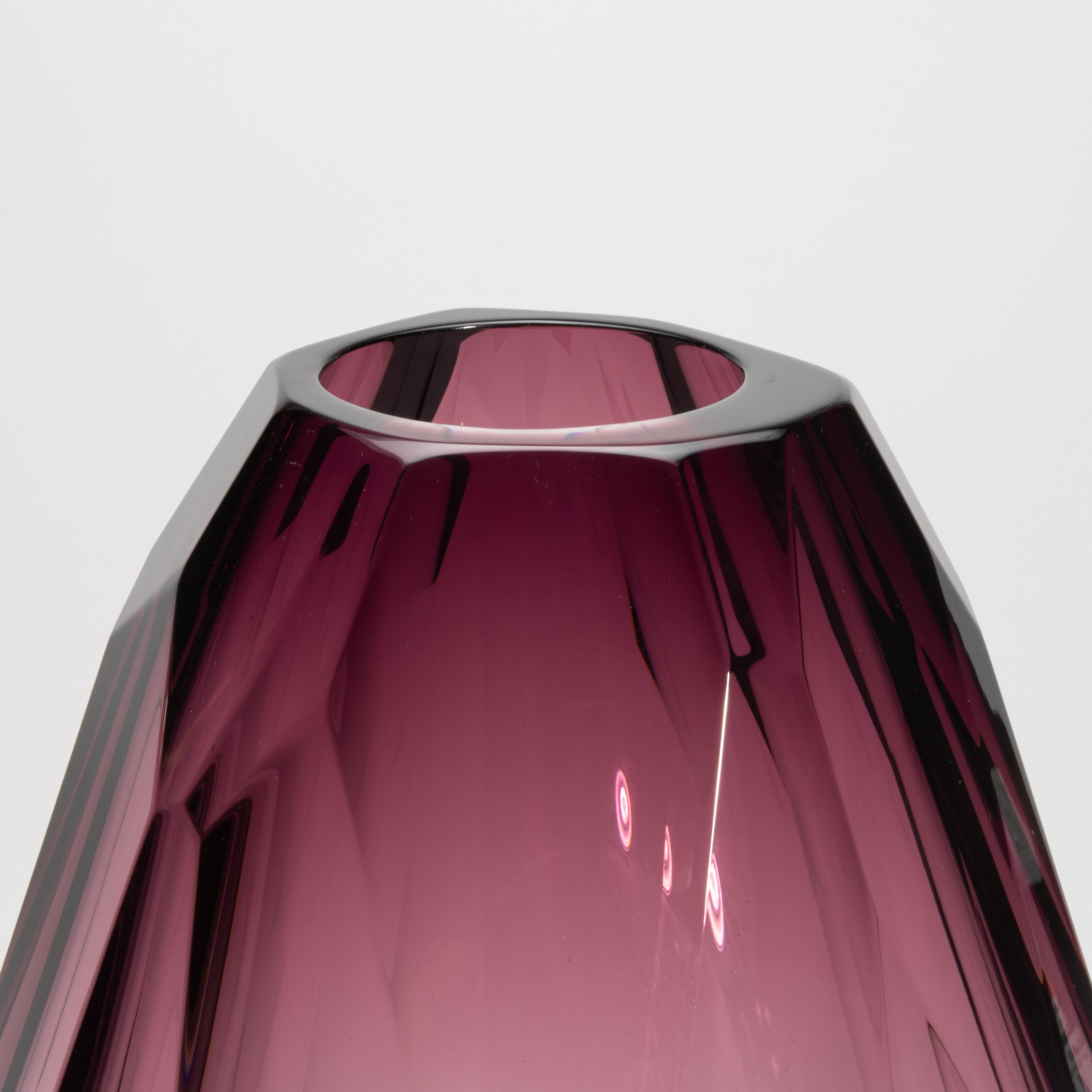 Un capolavoro di eleganza scultorea, questo vaso extra alto soffiato a mano di Murano in colore ametista affascina con la sua silhouette sfaccettata e la sua traslucenza eterea. Ogni superficie, tagliata con precisione geometrica, cattura e rifrange