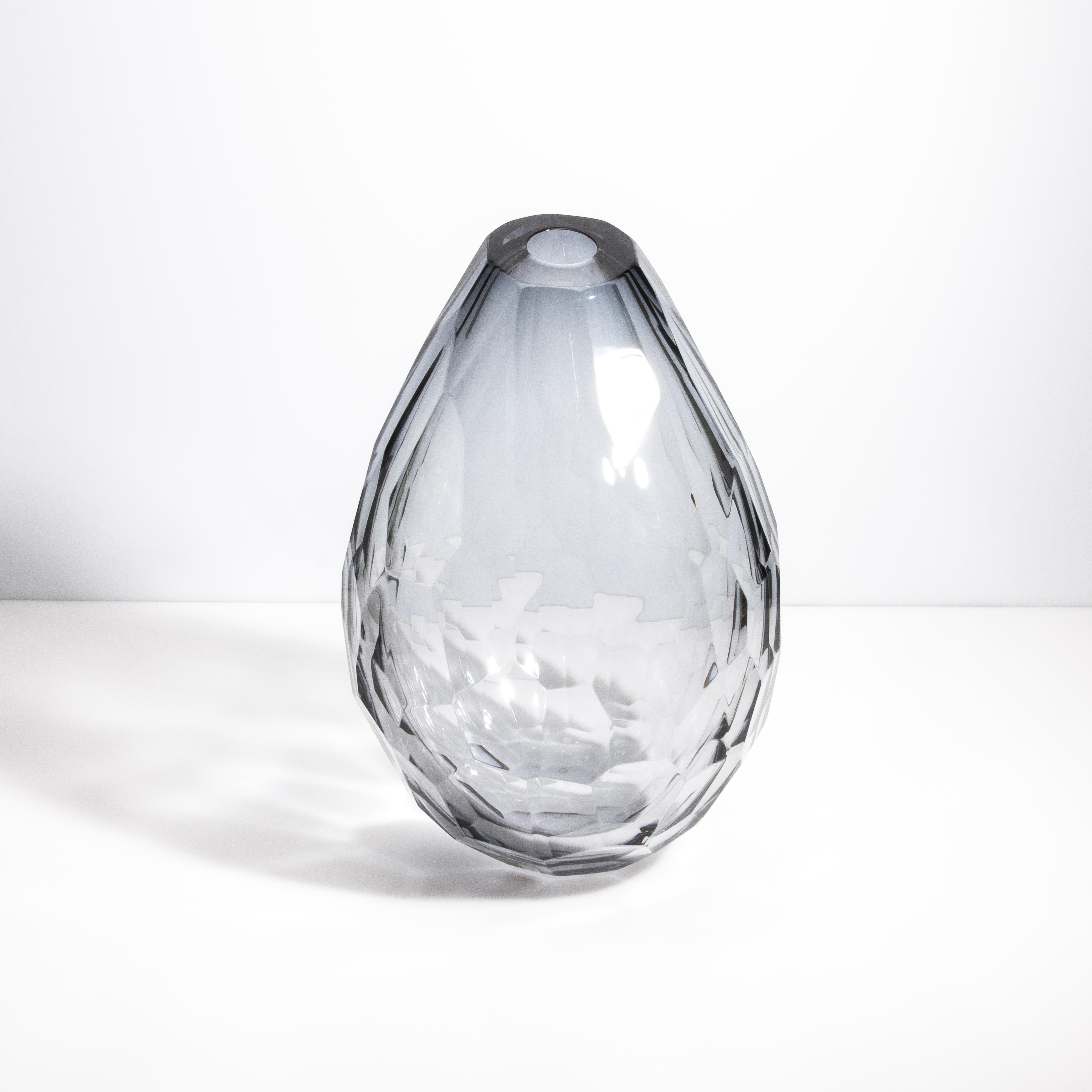 Diese luxuriöse, facettierte Vase ist ein wahres Meisterwerk der zeitgenössischen Murano-Glaskunst. Das makellos klare Glas mit einem dezenten Grauton ist fein facettiert und erzeugt ein schillerndes, diamantartiges Aussehen, das das Licht wunderbar
