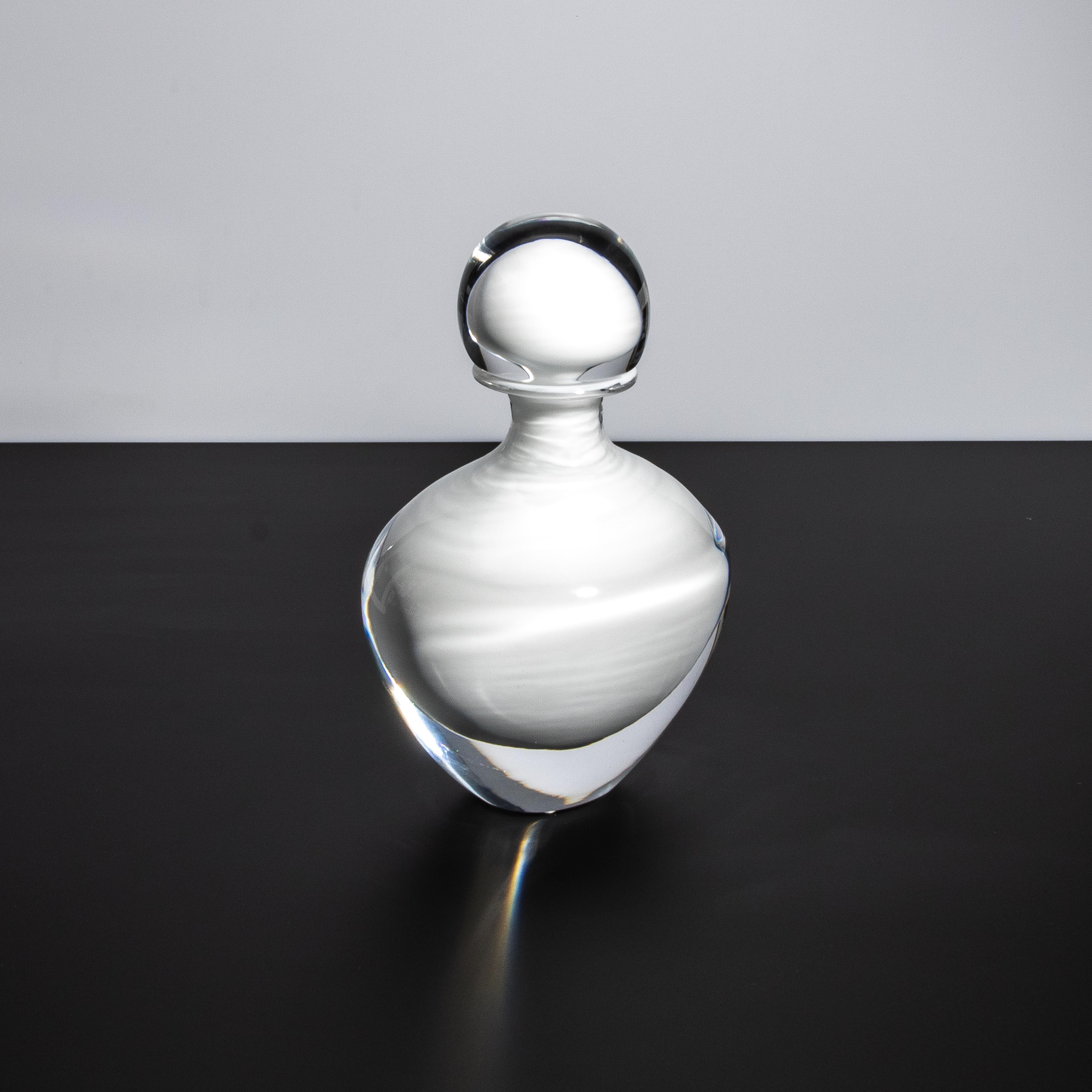 Ti presentiamo l'epitome dell'eleganza e della raffinatezza: la bottiglia di Murano soffiata a mano in un'immacolata finitura di cristallo chiaro, arricchita da un etereo elemento in vetro bianco. Questo squisito pezzo mette in mostra