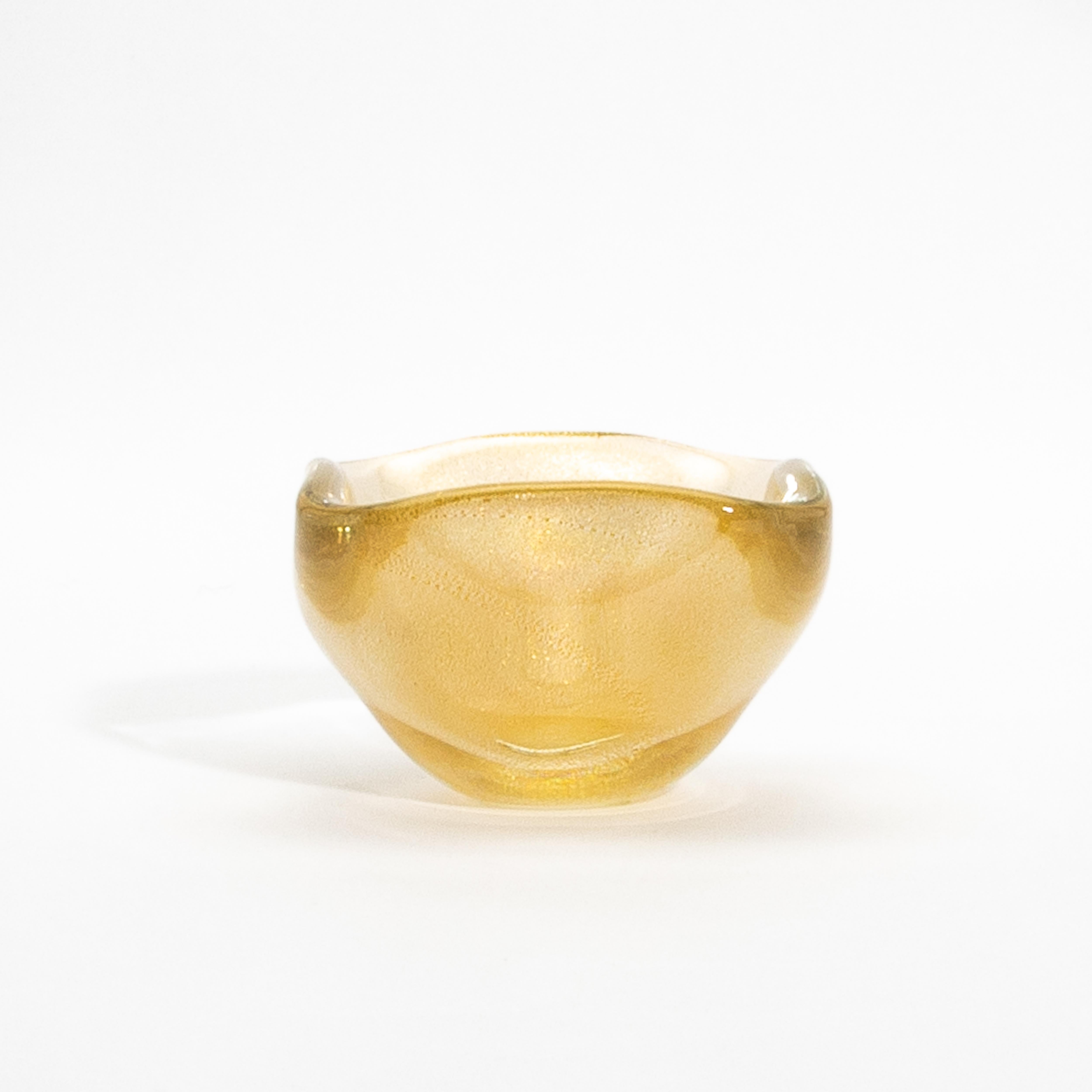 Questa squisita ciotola di Murano soffiata a mano è un capolavoro luminoso, con macchie d'oro a 24 carati che brillano all'interno del suo delicato vetro dorato. Realizzato con tecniche veneziane senza tempo, questo pezzo unico combina una