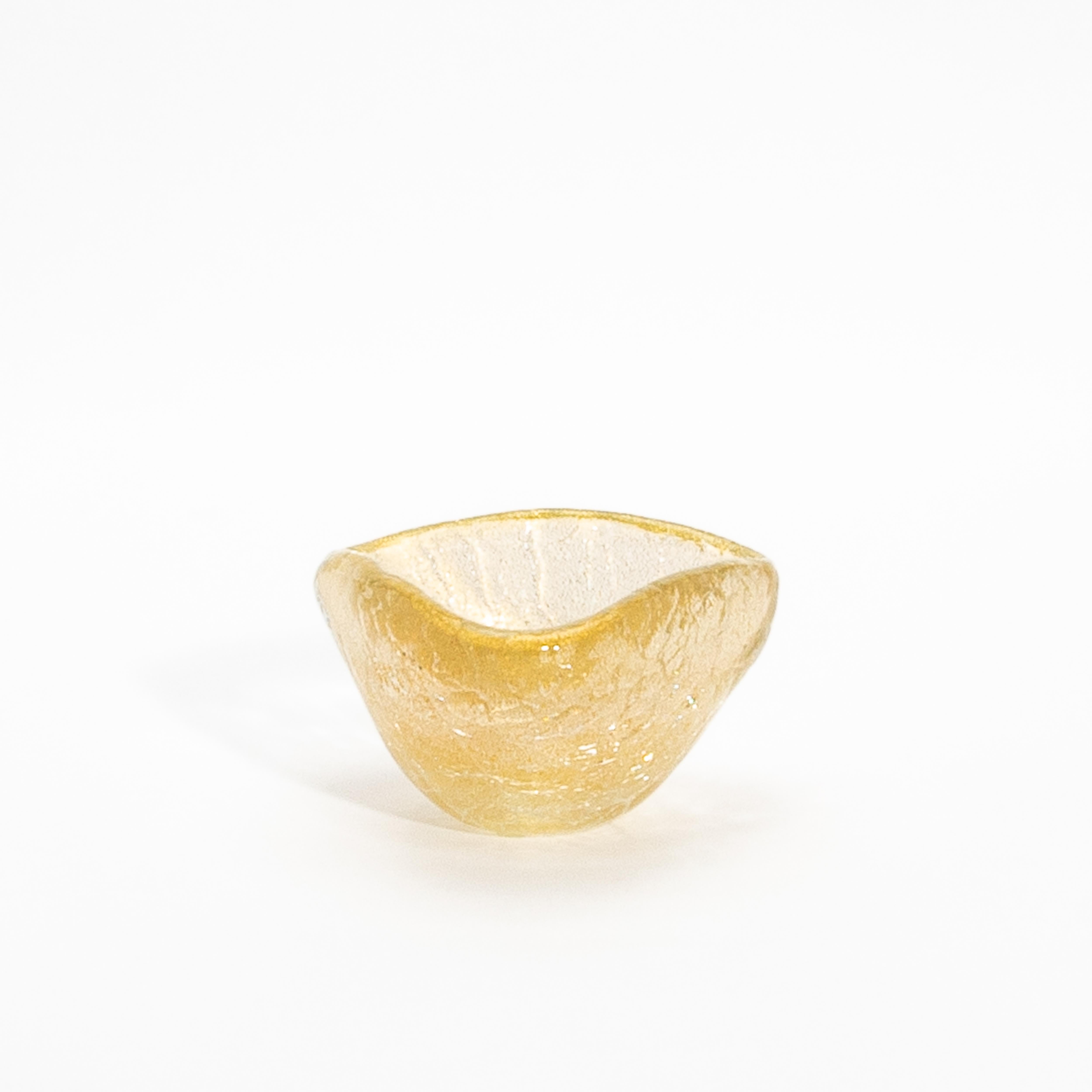 Delicadamente soplado a mano por maestros artesanos de Murano, este cuenco es un testimonio de la elegancia y la herencia de la cristalería veneciana. Su forma orgánica se acentúa con un lustroso tono dorado, impregnado de brillantes motas de oro de