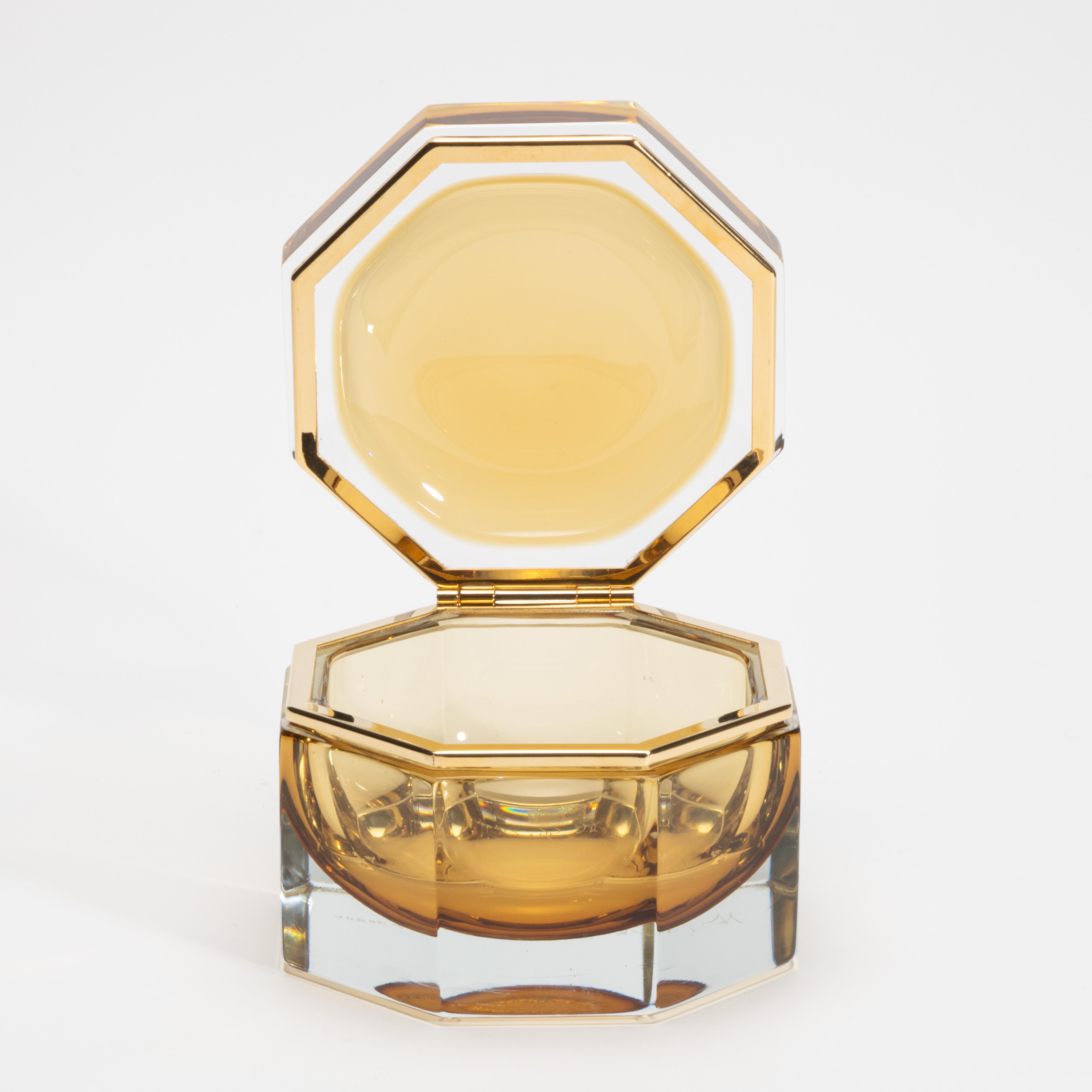 Diese mundgeblasene Murano-Dose aus tiefem Tabakglas verkörpert eine stille Opulenz, die mit skulpturaler Präzision und zeitloser Raffinesse gefertigt wurde. Die achteckige Silhouette ist markant und raffiniert zugleich. Die facettierten Kanten