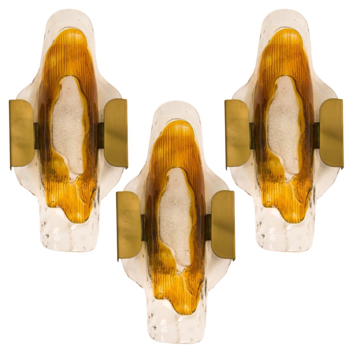 One of three beautiful wall lights, manufactured in the Mid Century, circa 1970 (end of 1960s and beginning of 1970s).
A brass frame and a bi-colored (clear and orange/ambre ) hand blown Murano glass. Each piece of glass meticulously hand formed in