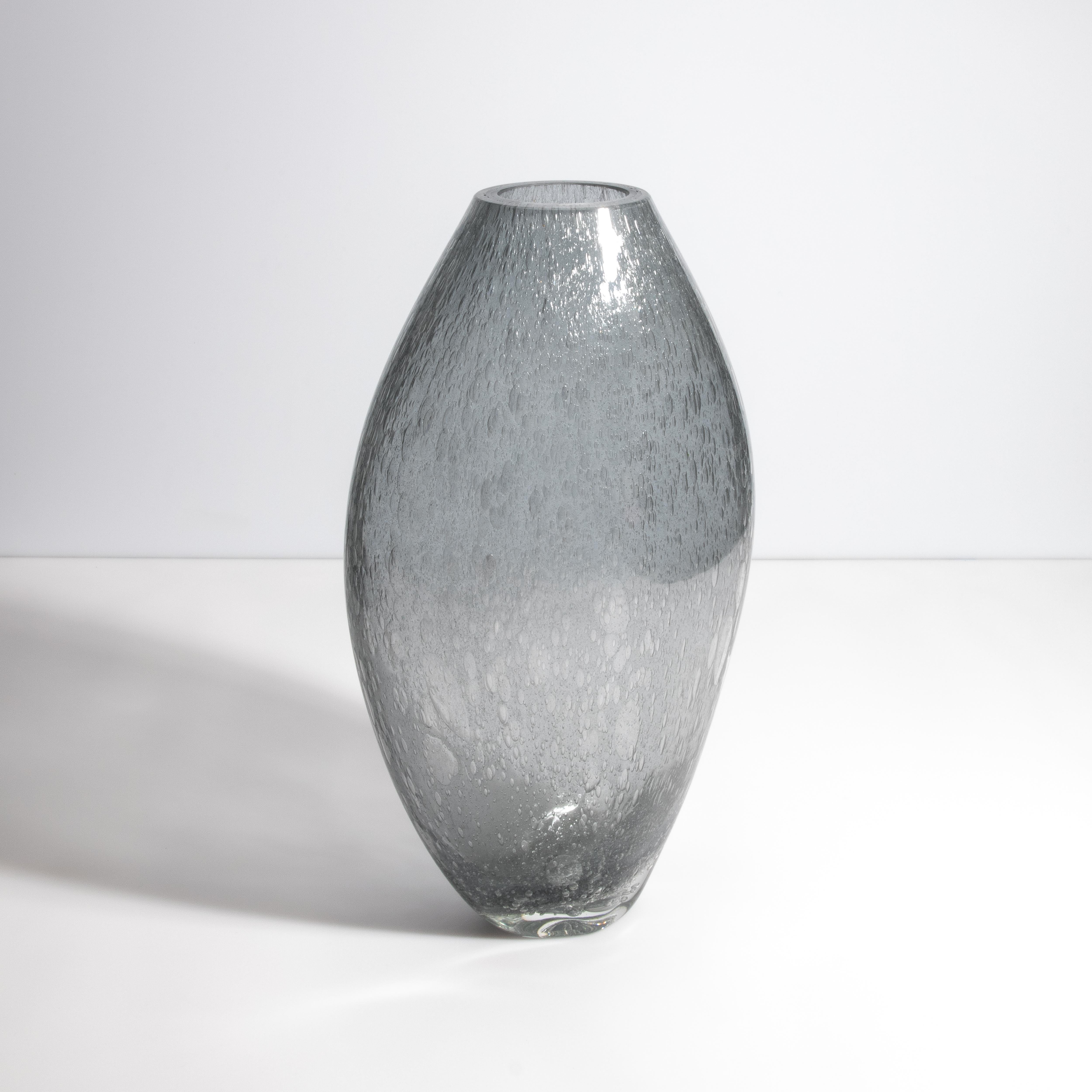 Scopri la serena eleganza di questa opera d'arte in vetro di Murano. Il delicato gradiente di grigio del vaso ricorda la tranquilla bellezza di una laguna veneziana sotto un cielo nuvoloso. L'intricata tecnica della 