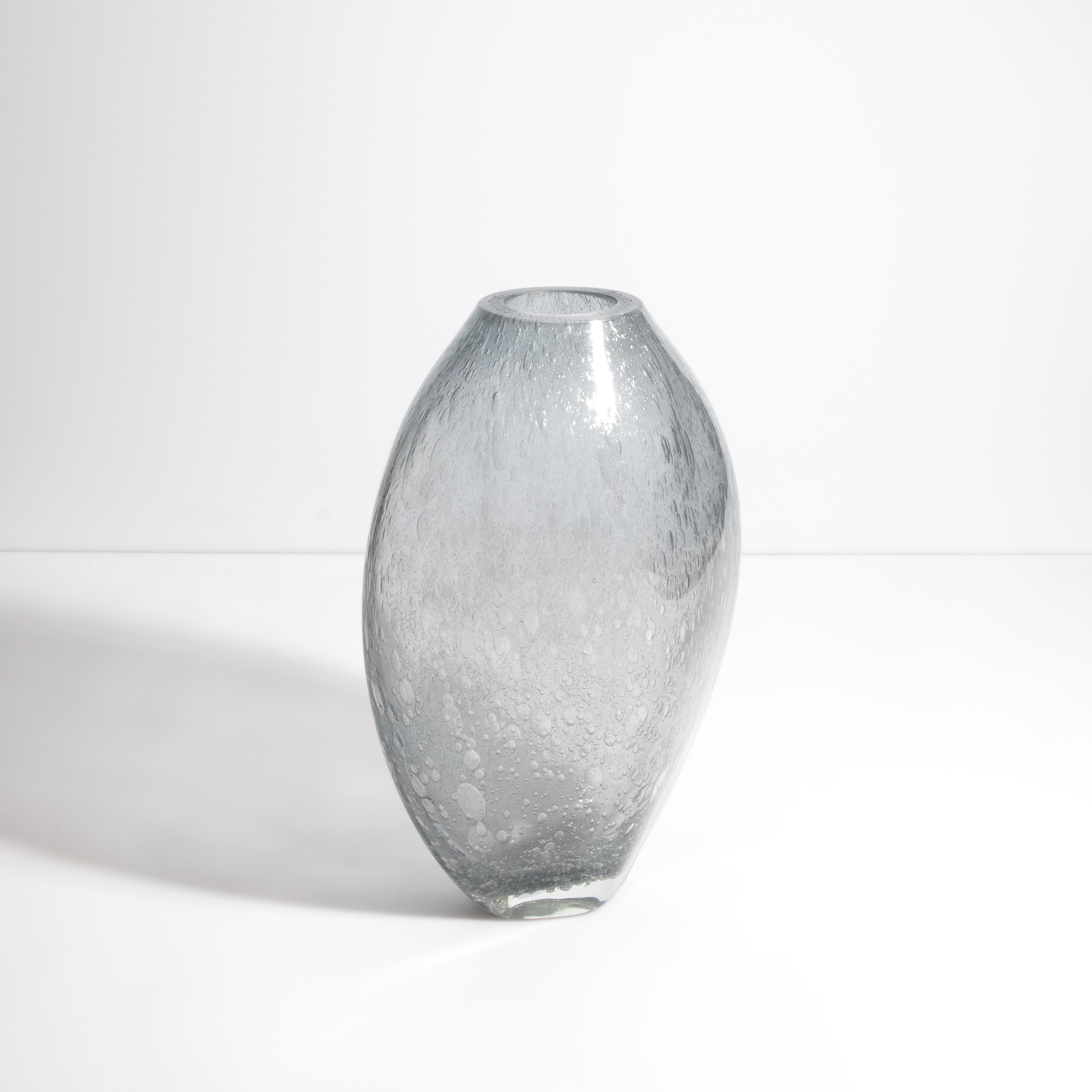Scopri la serena eleganza di questa opera d'arte in vetro di Murano. Il delicato gradiente di grigio del vaso ricorda la tranquilla bellezza di una laguna veneziana sotto un cielo nuvoloso. L'intricata tecnica della 