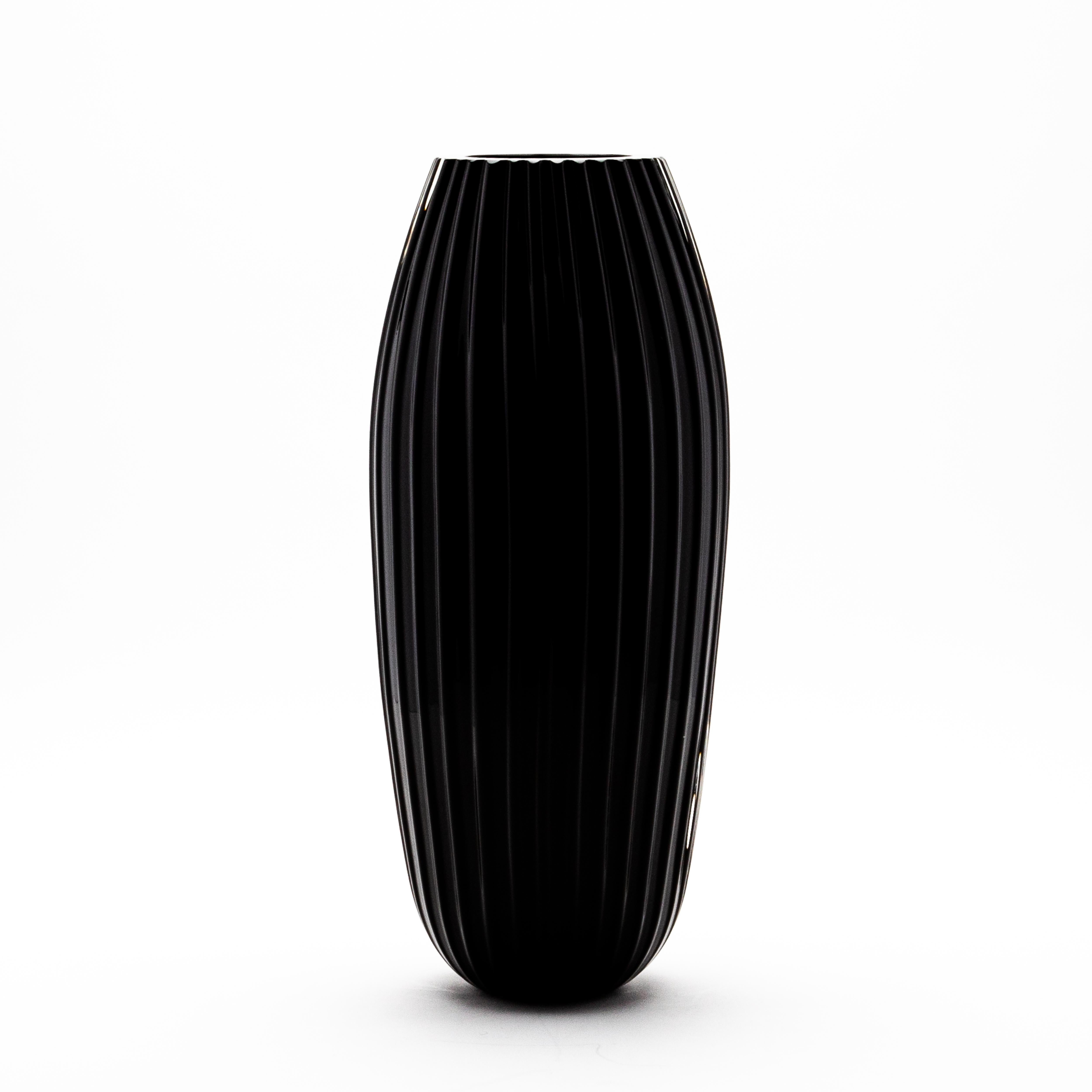 Questo vaso di Murano extra alto in nero onice è una celebrazione di un'eleganza senza tempo, realizzata dagli artigiani del vetro di Murano, famosi in tutto il mondo, con una precisione e un'abilità notevoli. La sua forma allungata e scanalata, che