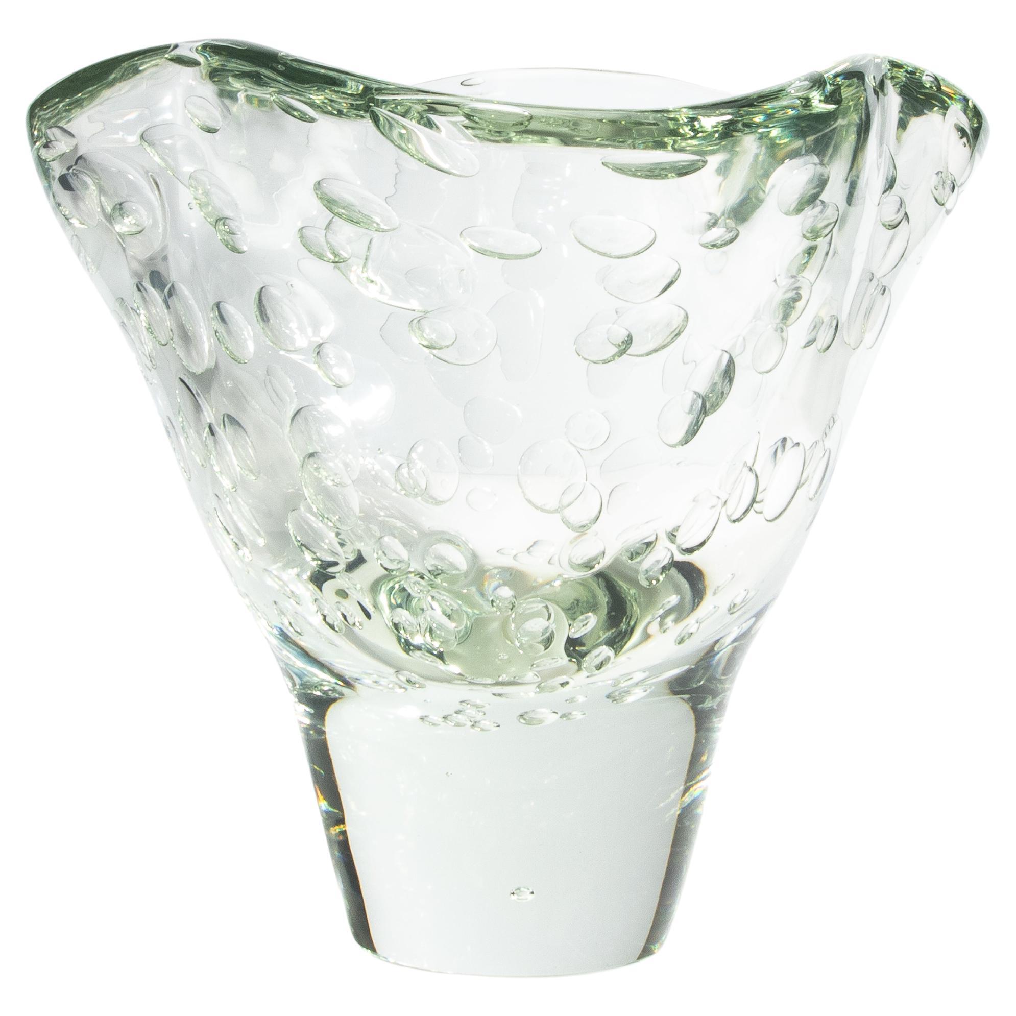 Questo vaso è uno straordinario pezzo d'arte in vetro di Murano, ispirato alla fluidità e al movimento dell'acqua. La sua forma organica e ondulata è accentuata dalla base in vetro trasparente, che crea un senso di leggerezza e delicatezza. La