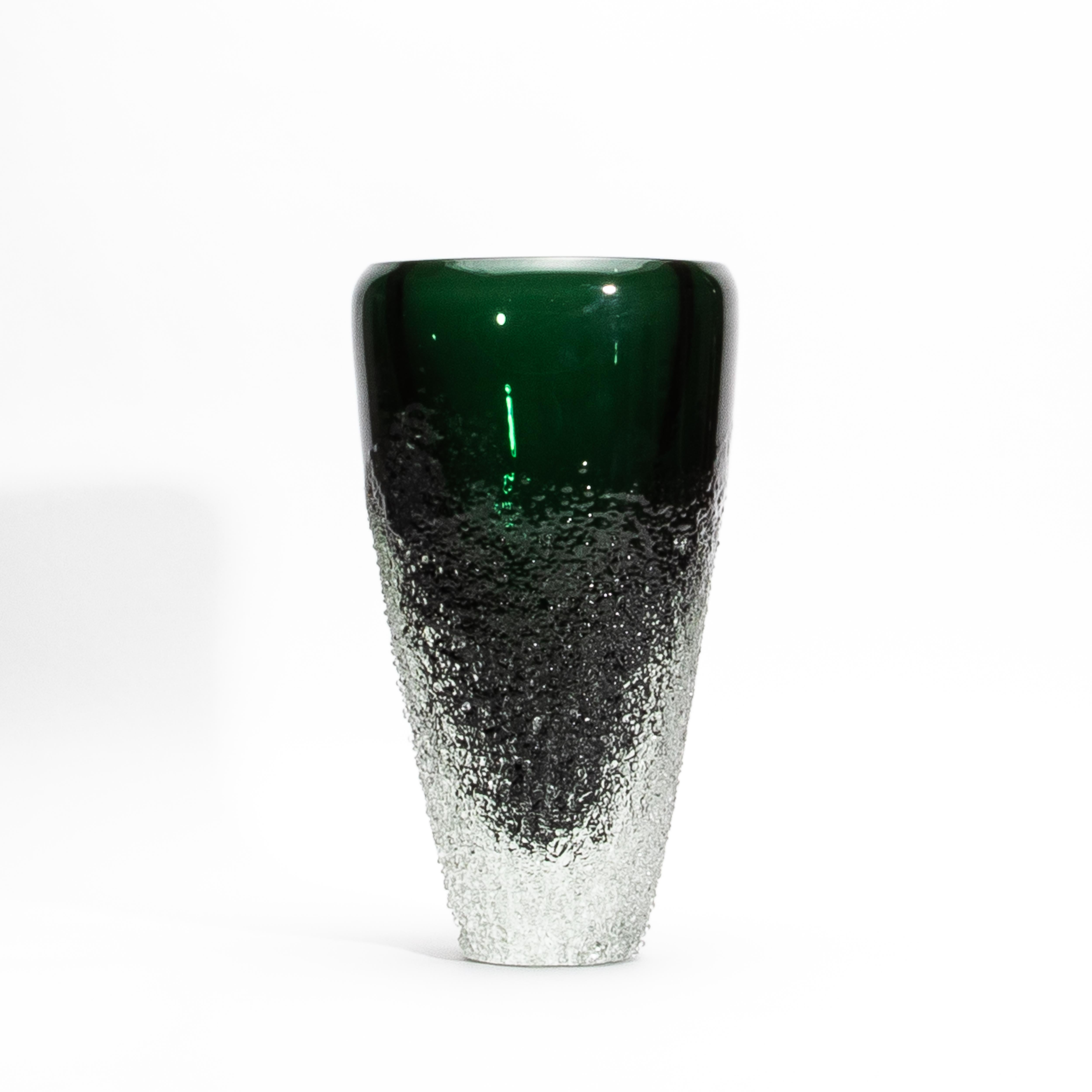 The Murano Frozen Vase in Emerald Green is a sculptural marvel, embodying the essence of refined design and intricate craftsmanship. Its deep emerald green surface flows seamlessly into a textured, icy base that evokes the raw beauty of frozen