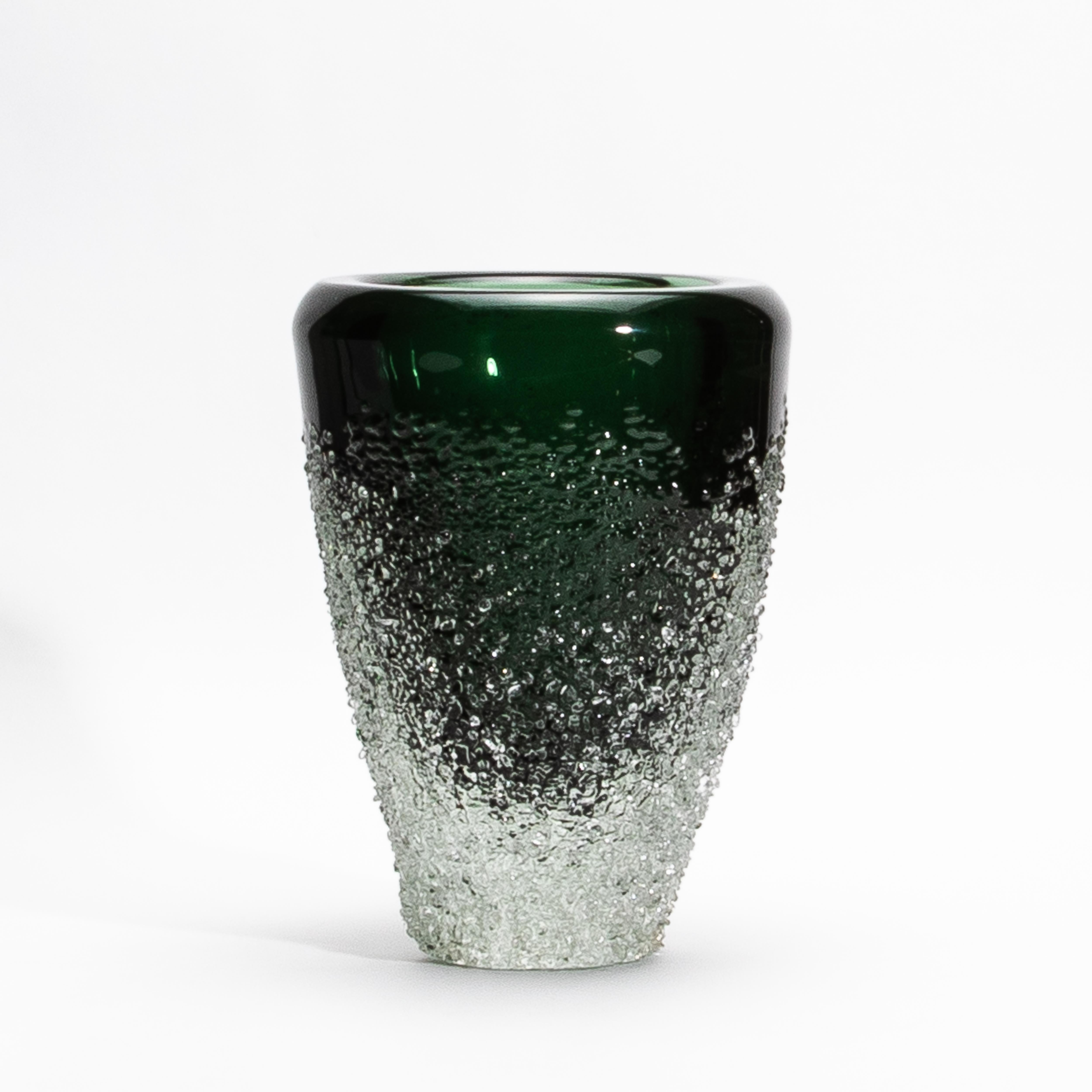 The Murano Frozen Vase in Emerald Green is a sculptural marvel, embodying the essence of refined design and intricate craftsmanship. Its deep emerald green surface flows seamlessly into a textured, icy base that evokes the raw beauty of frozen