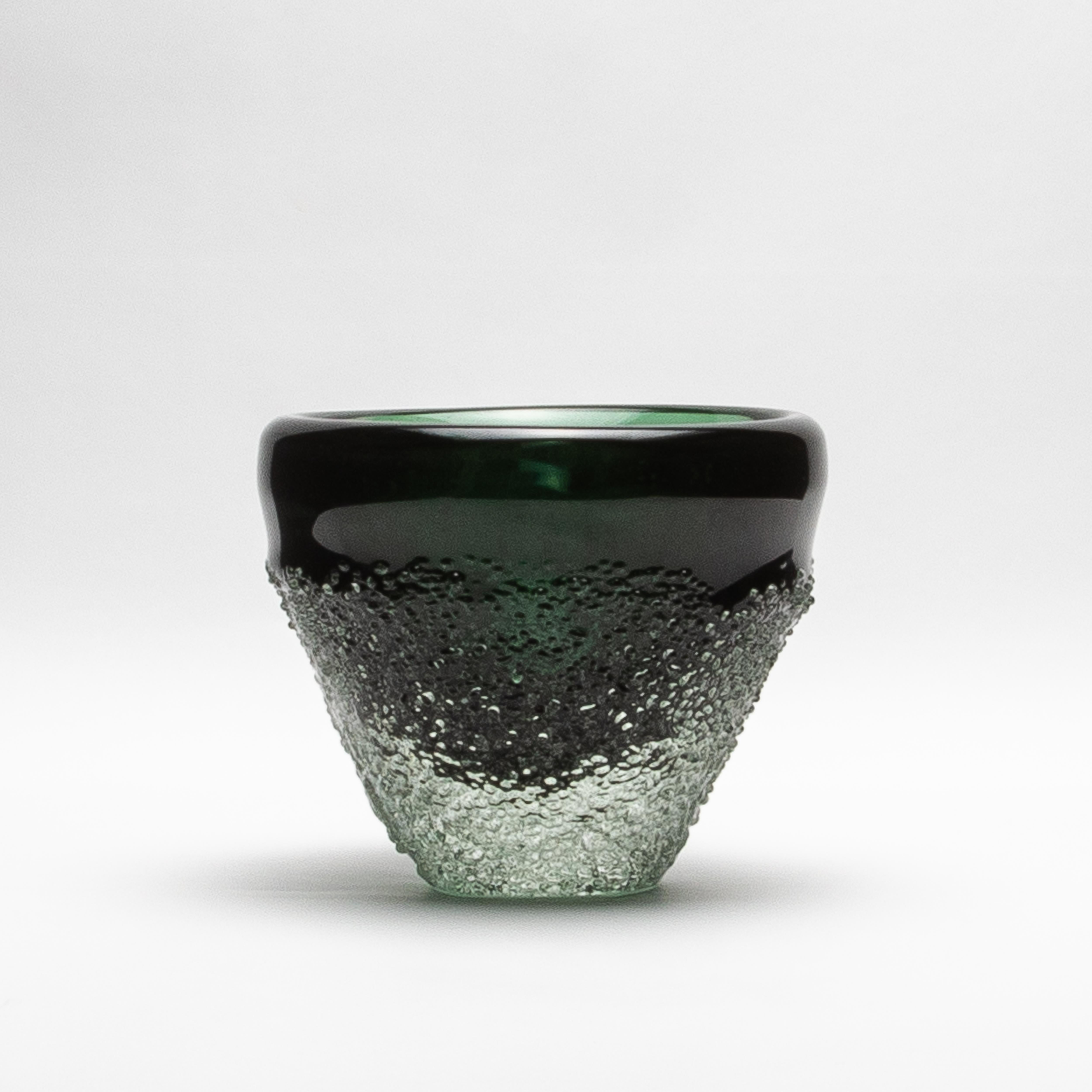 The Murano Frozen Vase in Emerald Green is a sculptural marvel, embodying the essence of refined design and intricate craftsmanship. Its deep emerald green surface flows seamlessly into a textured, icy base that evokes the raw beauty of frozen