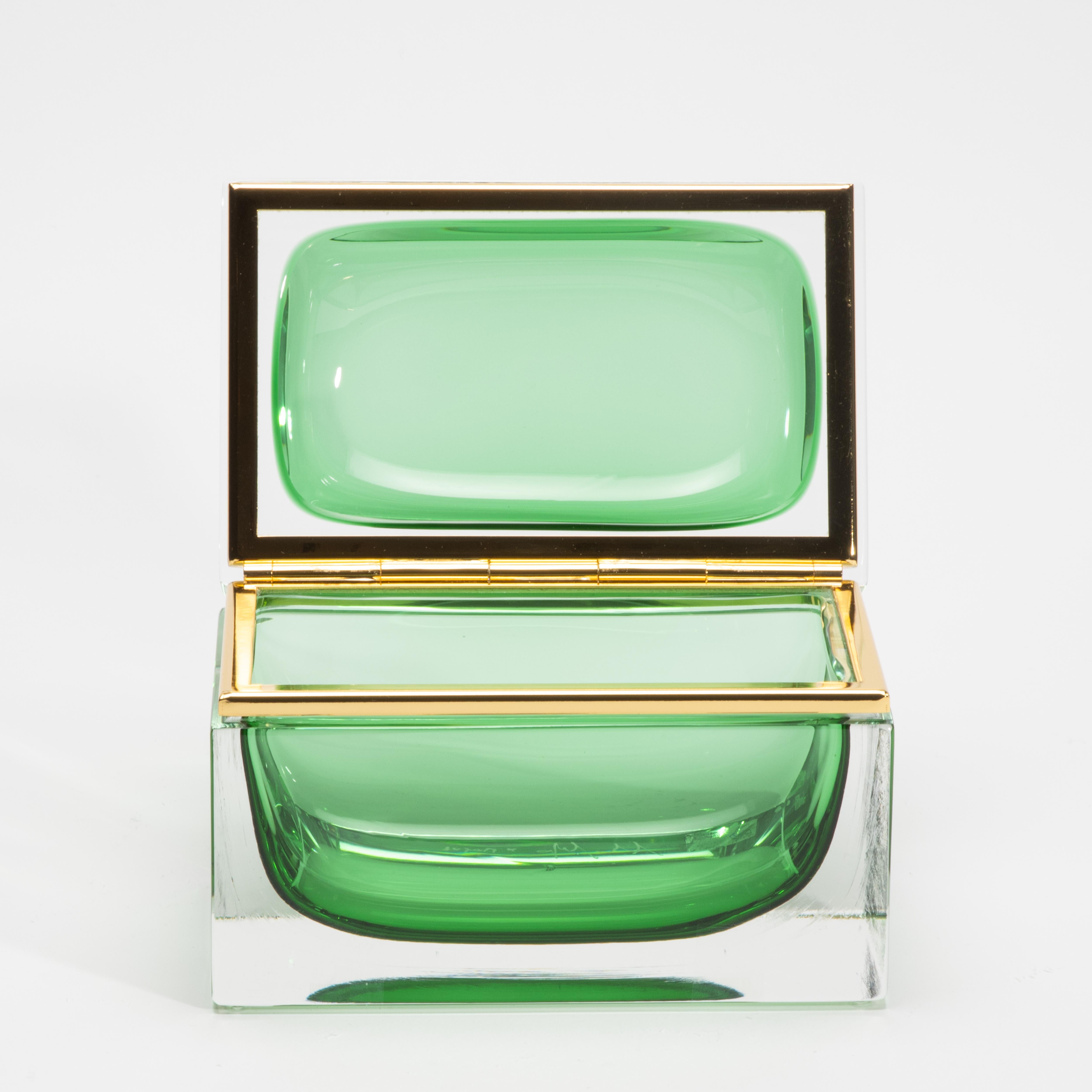 Objet d'une allure saisissante, cette boîte monumentale en verre de Murano rayonne de raffinement par sa géométrie sculpturale et sa teinte émeraude richement saturée. La clarté de la base en cristal soufflé à la main embrasse un intérieur vert