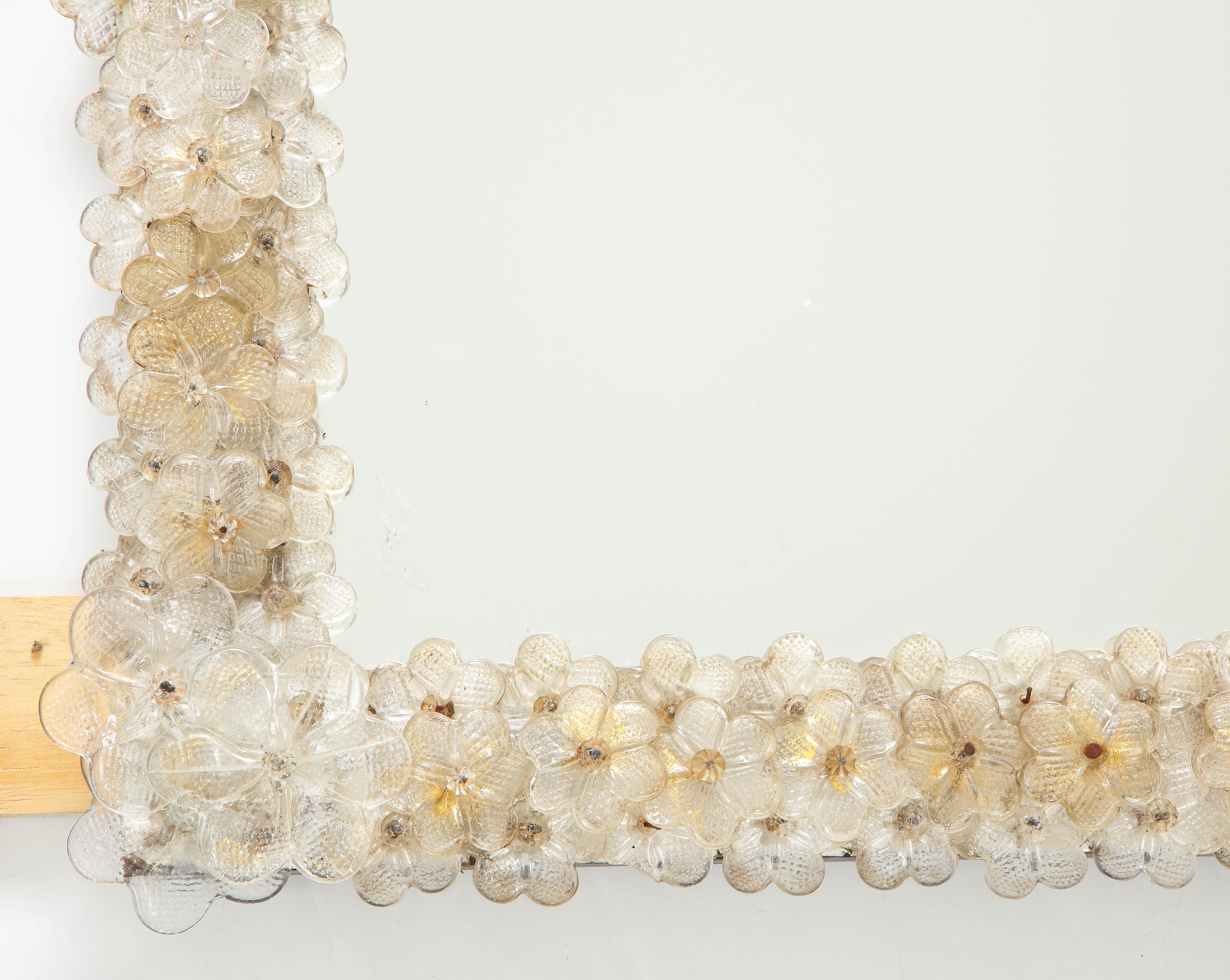 A beautiful entirely handcrafted blown Murano glass wall mirror, designed and made on Murano in Venice in the 1950s. The frame of the mirror is elaborately decorated with multi-layered handcrafted Murano glass flowers, clear and speckled with gold,