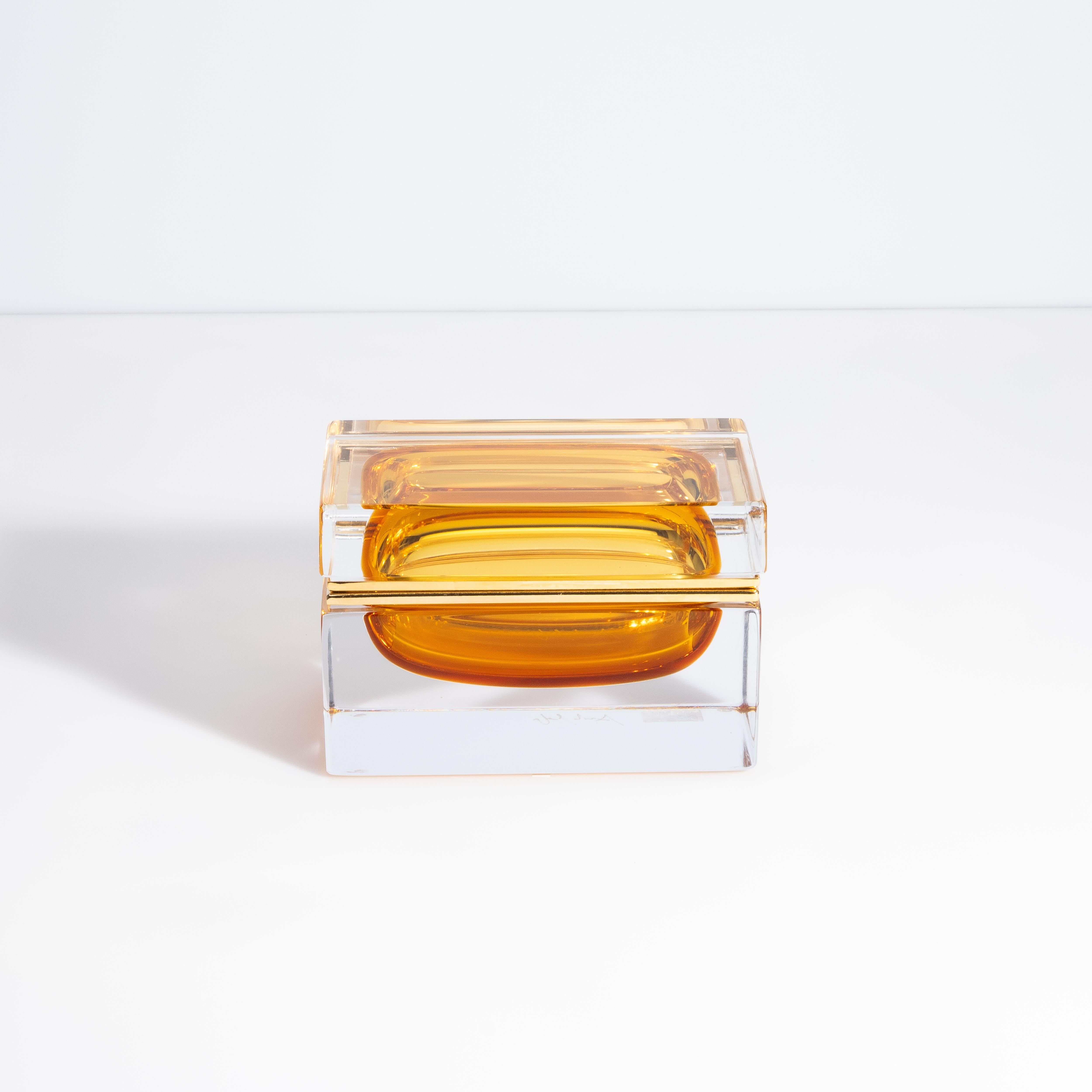 La infusión de ámbar dorado confiere un encanto fascinante a esta encantadora caja de cristal soplado a mano, procedente de Murano, Italia. La calidez evoca una sensación de lujo y sofisticación, que es un absoluto deleite para la vista. En efecto,