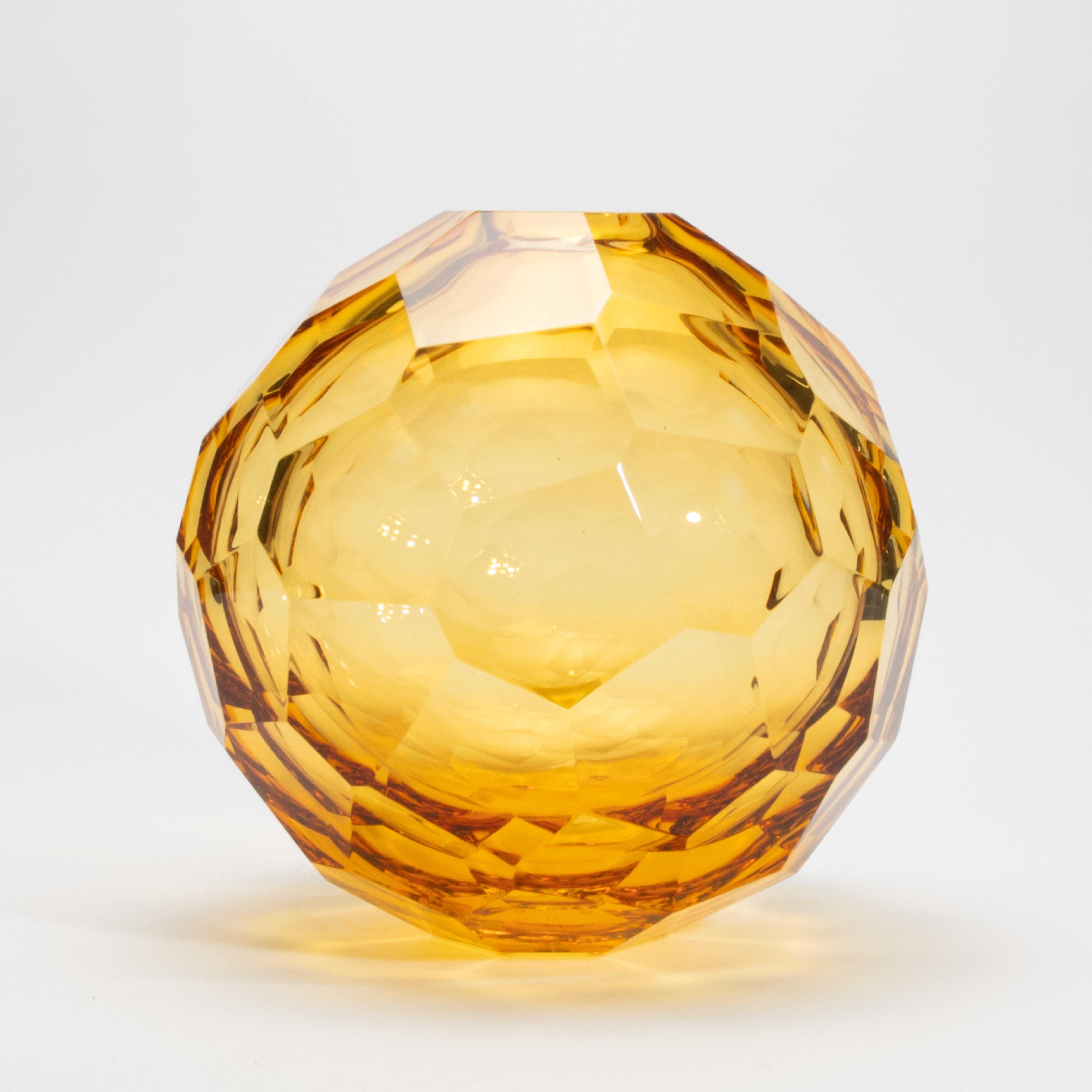 Diese mundgeblasene Murano-Kugelvase aus Bernstein ist eine strahlende Studie über Licht und Form und strahlt Wärme, Brillanz und handwerkliche Präzision aus. Seine facettenreiche Silhouette wurde sorgfältig so geschliffen, dass sie das Licht wie