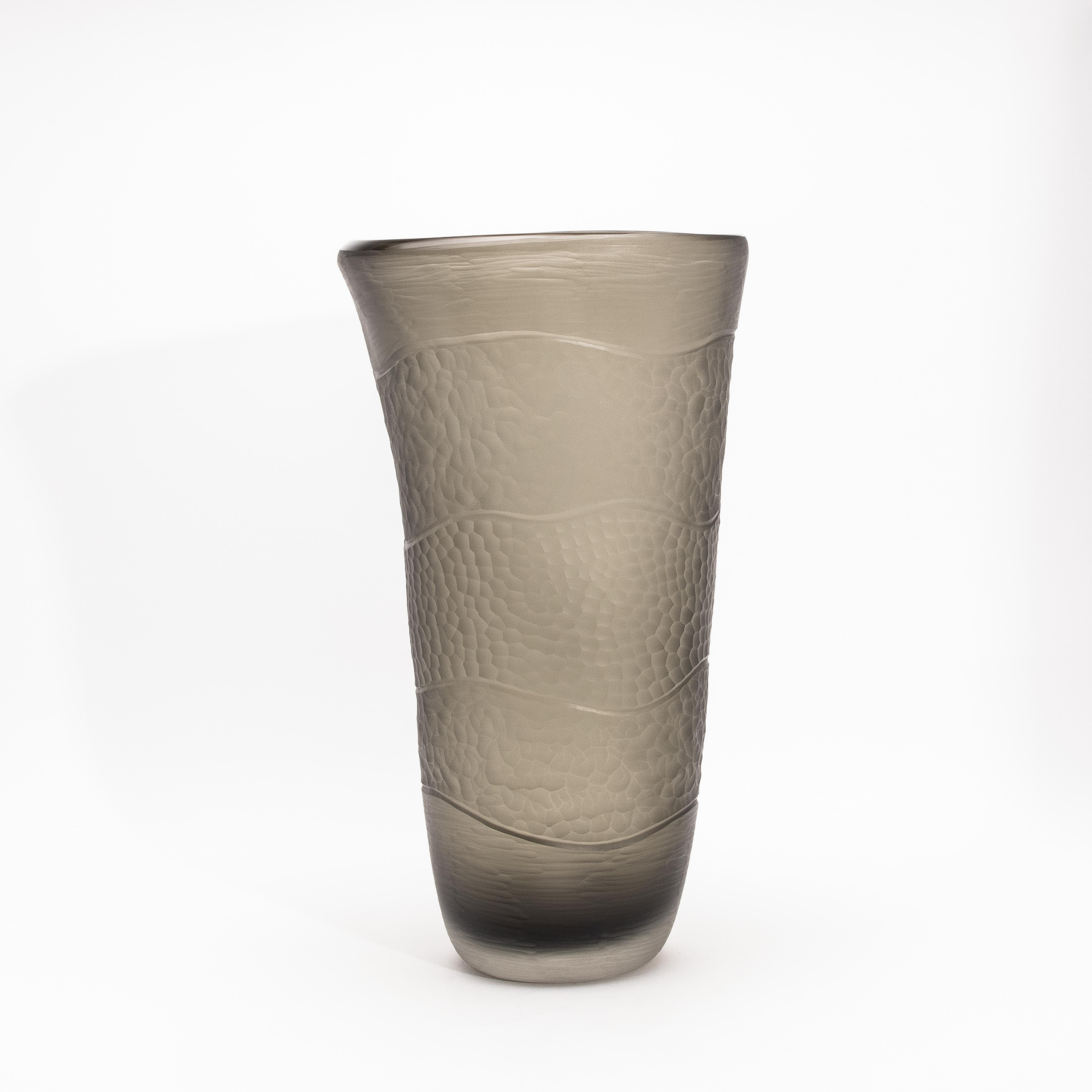 Etereo e scultoreo, questo vaso di Murano soffiato a mano attira l'attenzione con la sua altezza statuaria di 21 pollici e la sua texture seducente. Realizzato in un sofisticato gradiente di grigio fumo, il pezzo presenta bande ondulate che si