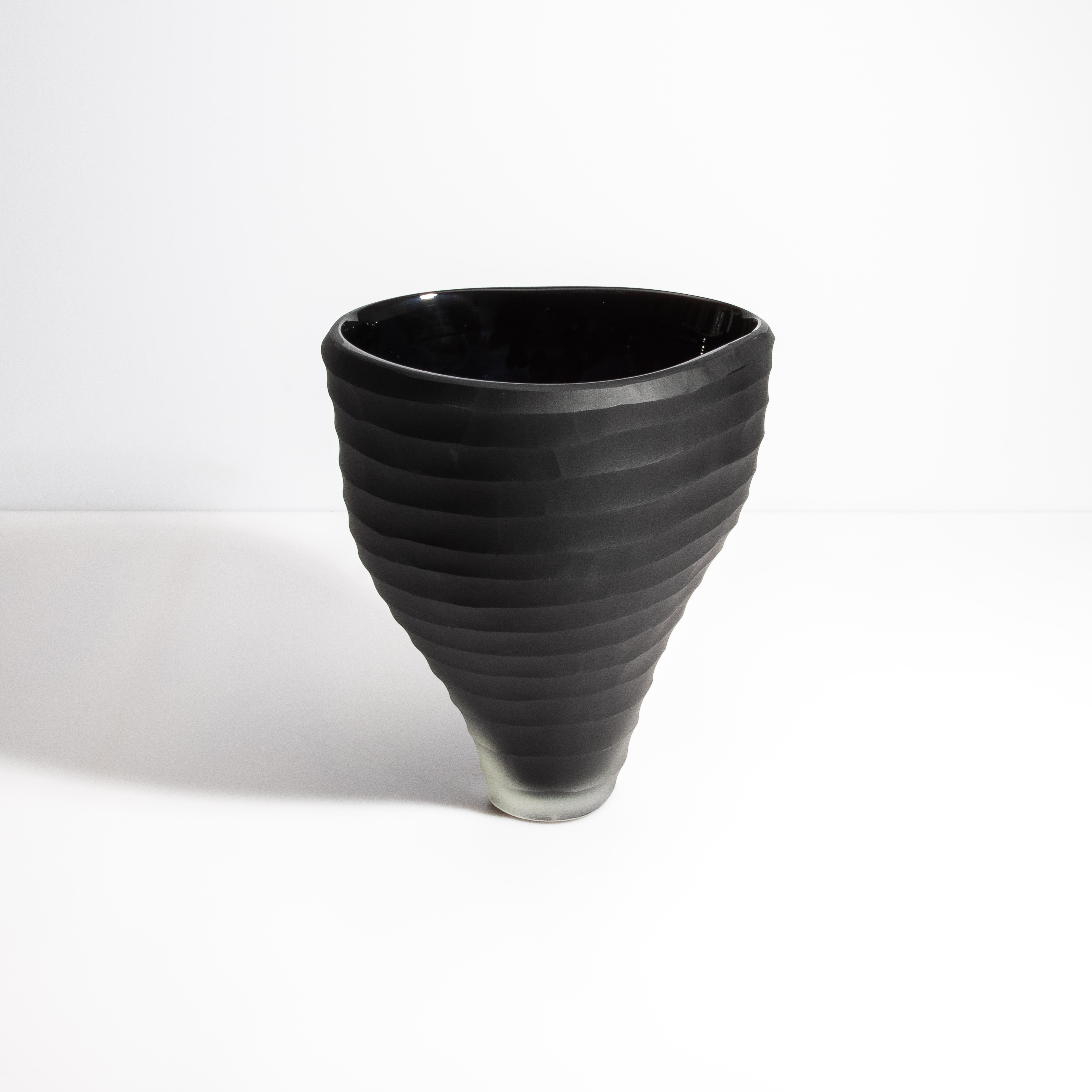 Cette pièce exquise illustre l'art moderne avec sa finition noire mate sophistiquée et sa forme aux contours uniques. Le vase présente une élégante forme conique qui s'affine gracieusement d'un large bord à une base étroite et givrée. Son extérieur