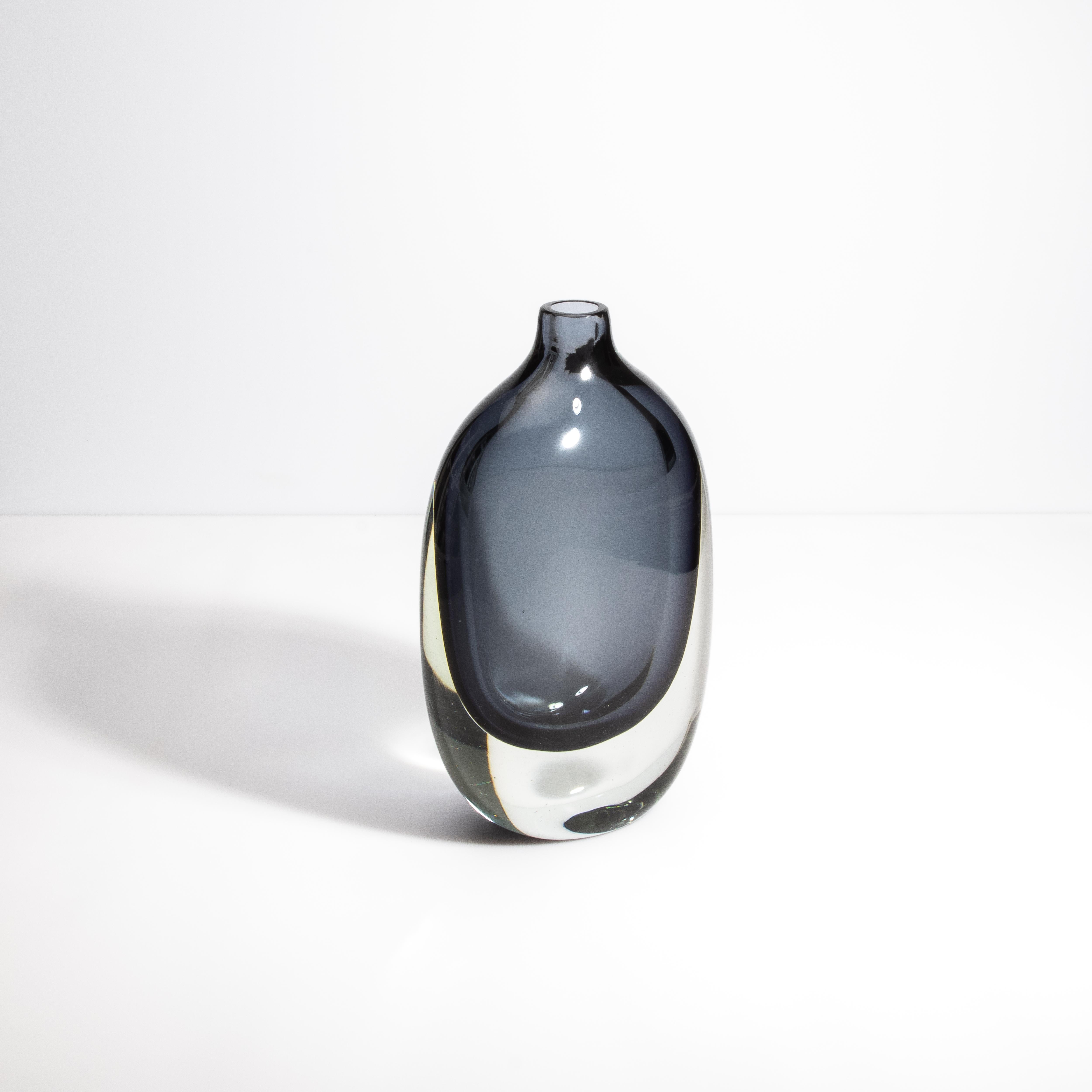 Inspiré par la grandeur de l'architecture italienne et l'élégance du design moderne, ce vase de Murano dégage un charme sophistiqué. L'interaction entre le verre gris et le verre transparent crée un mélange harmonieux, évoquant la brume sereine des