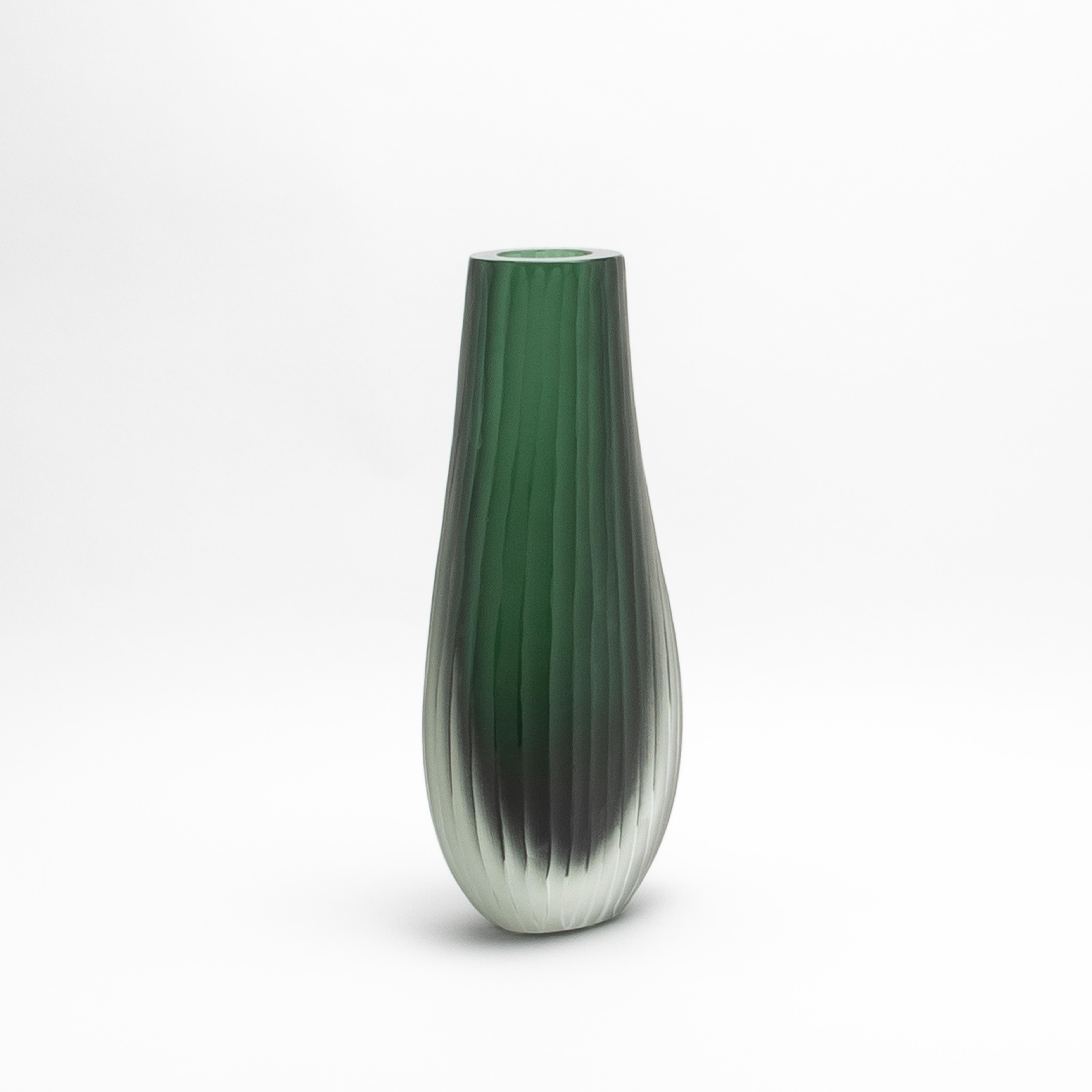 Il Vaso Supremo di Murano soffiato a mano in verde smeraldo emana un'eleganza senza tempo, fondendo vetro smerigliato e trasparente in un capolavoro armonioso. La sua texture delicatamente rigata crea un gioco dinamico di luci e ombre, accentuando