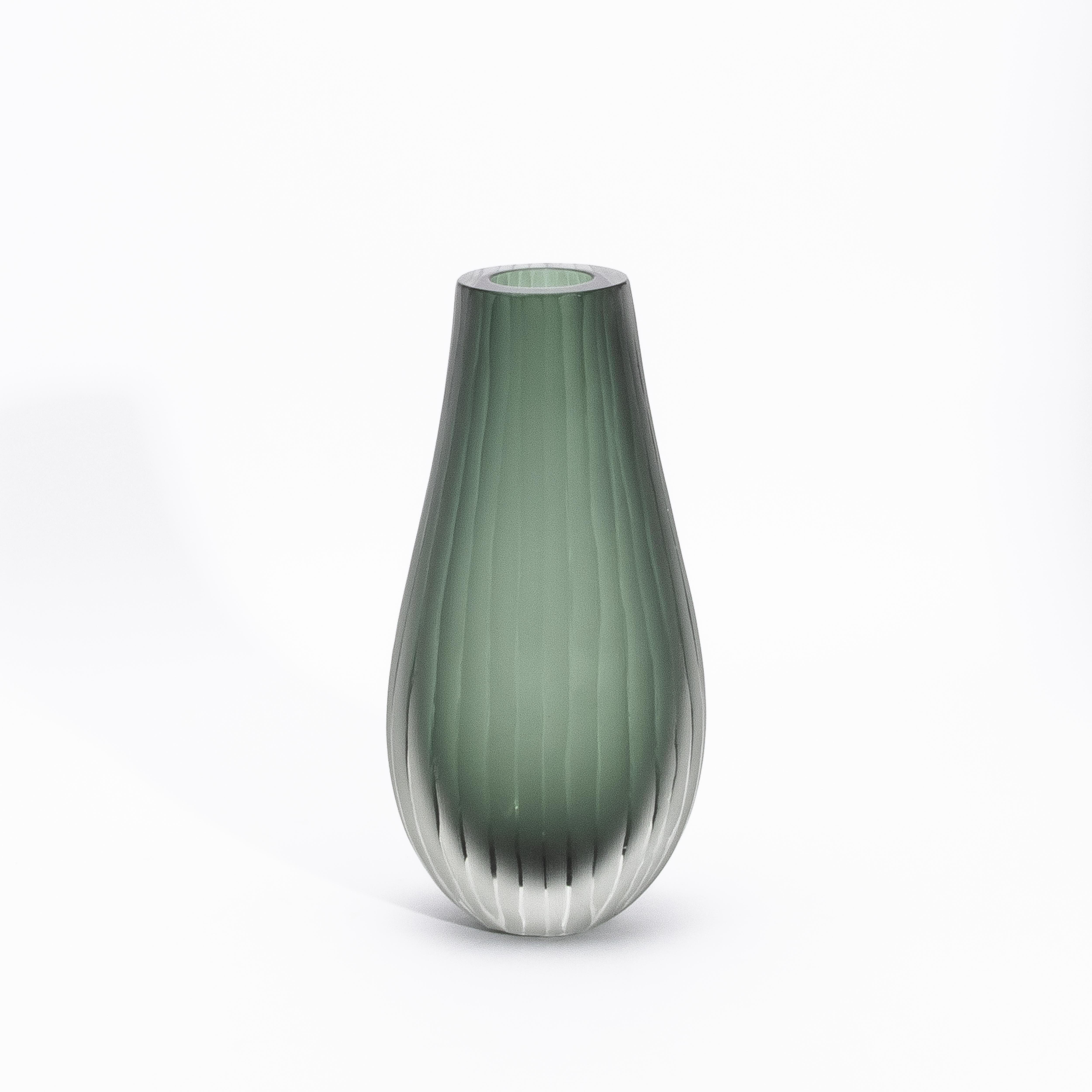 Elegante e scultoreo, il vaso Surpime in verde eucalipto è una testimonianza della bellezza poetica del vetro di Murano soffiato a mano. La sua silhouette - alta, dolcemente affusolata e delicatamente svasata sul labbro - evoca la raffinata