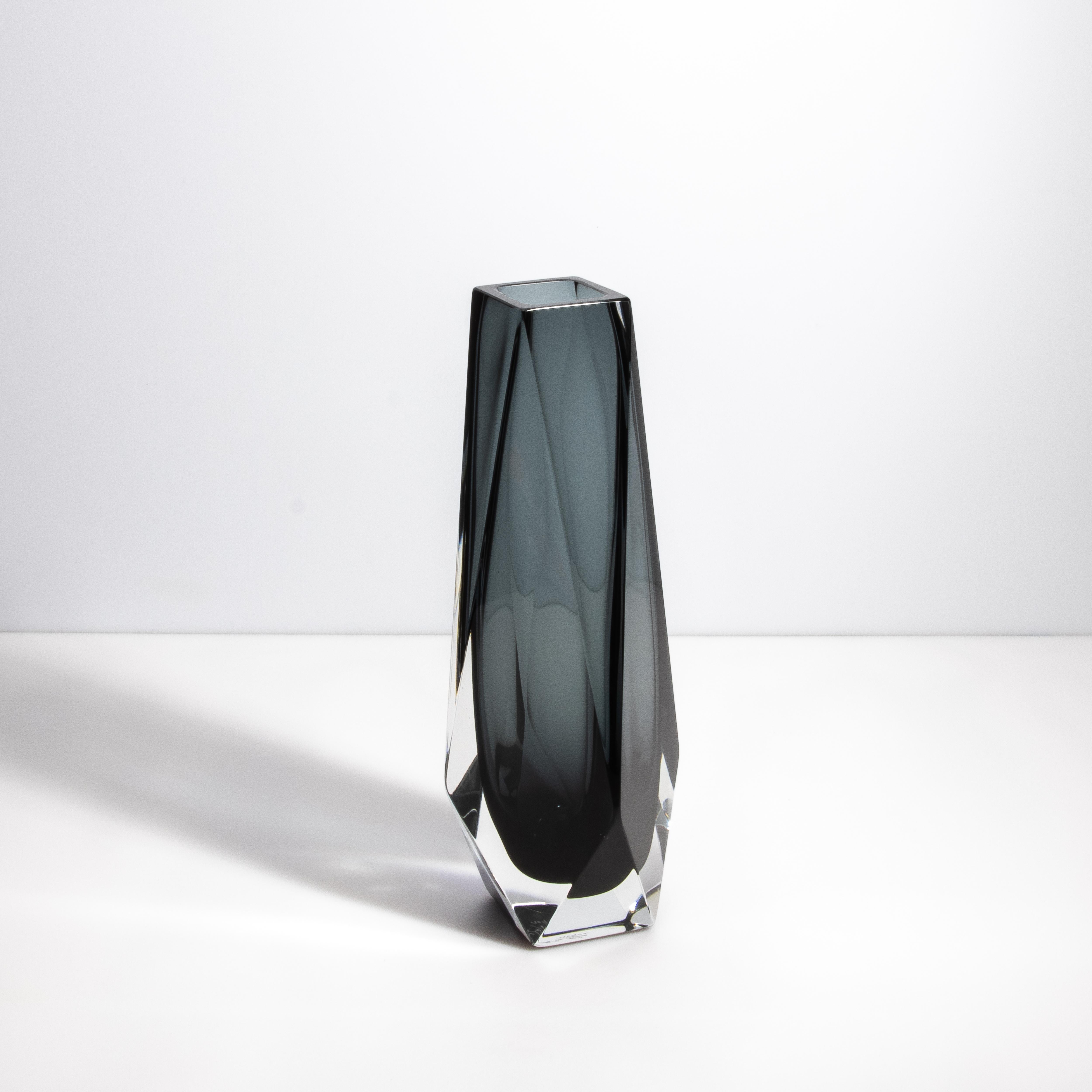 Questo vaso di Murano emana un fascino contemporaneo, fondendo la precisione geometrica con l'ispirazione organica di una goccia di pioggia. Realizzato da maestri vetrai, questo pezzo presenta una sorprendente tonalità di grigio intenso, incastonata