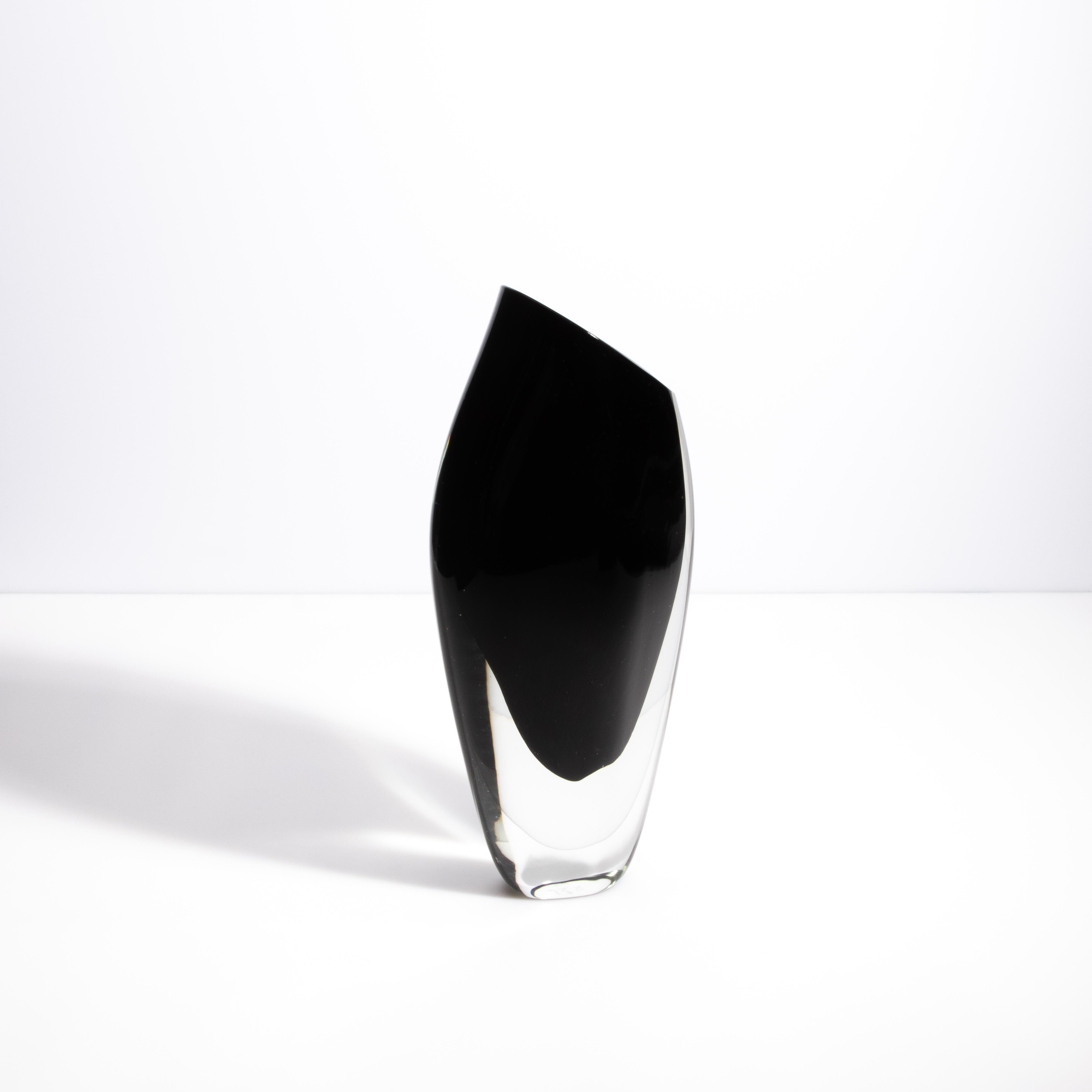 Questo elegante vaso in vetro di Murano incarna la raffinatezza e l'arte senza tempo dei vetrai veneziani. La sua tonalità nera profonda, in contrasto con i bordi in vetro cristallino, evoca un senso di lusso moderno. La silhouette elegante e